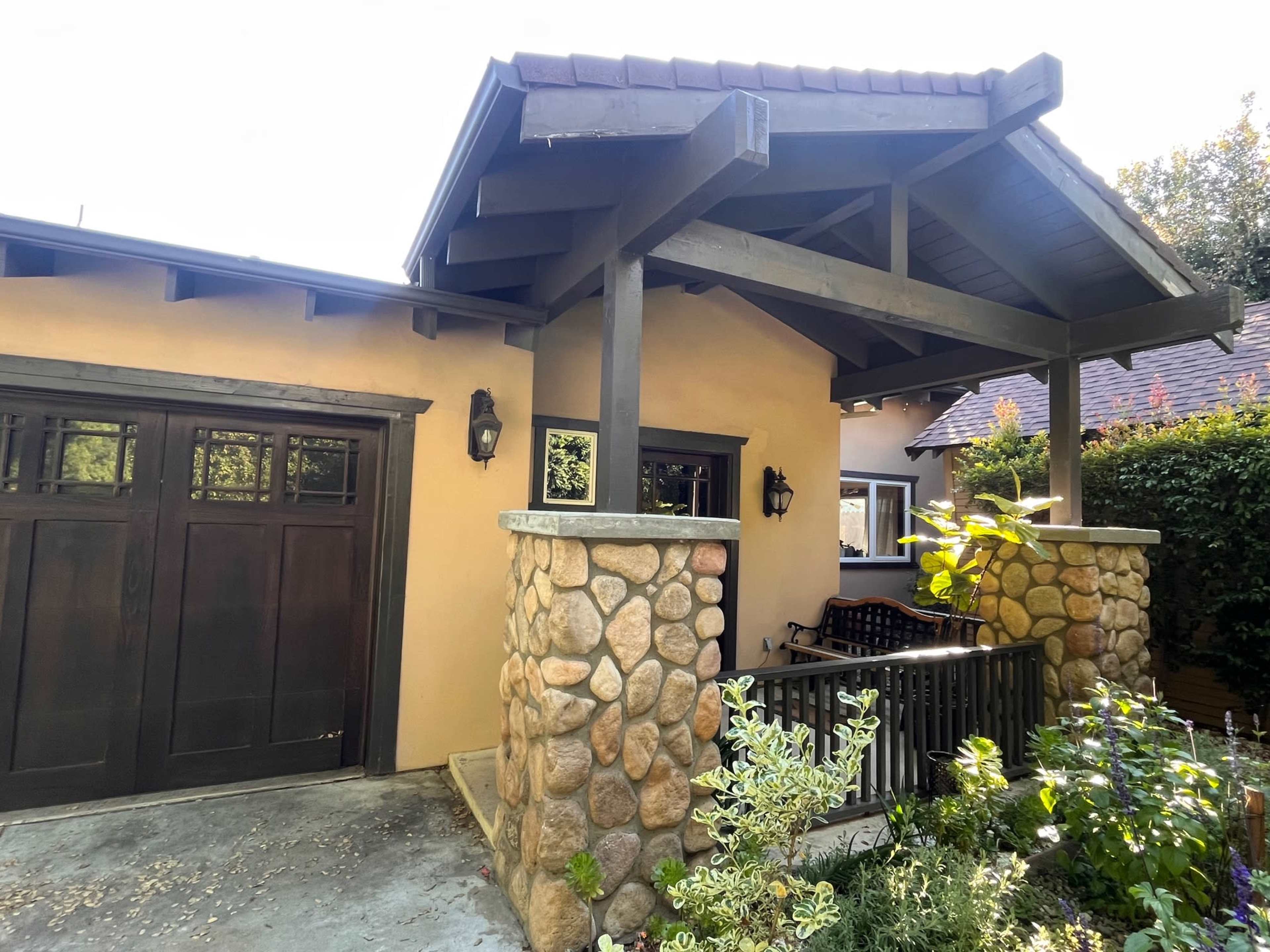 The image shows a house with a stone and wooden entryway, featuring a covered porch and a garage door.