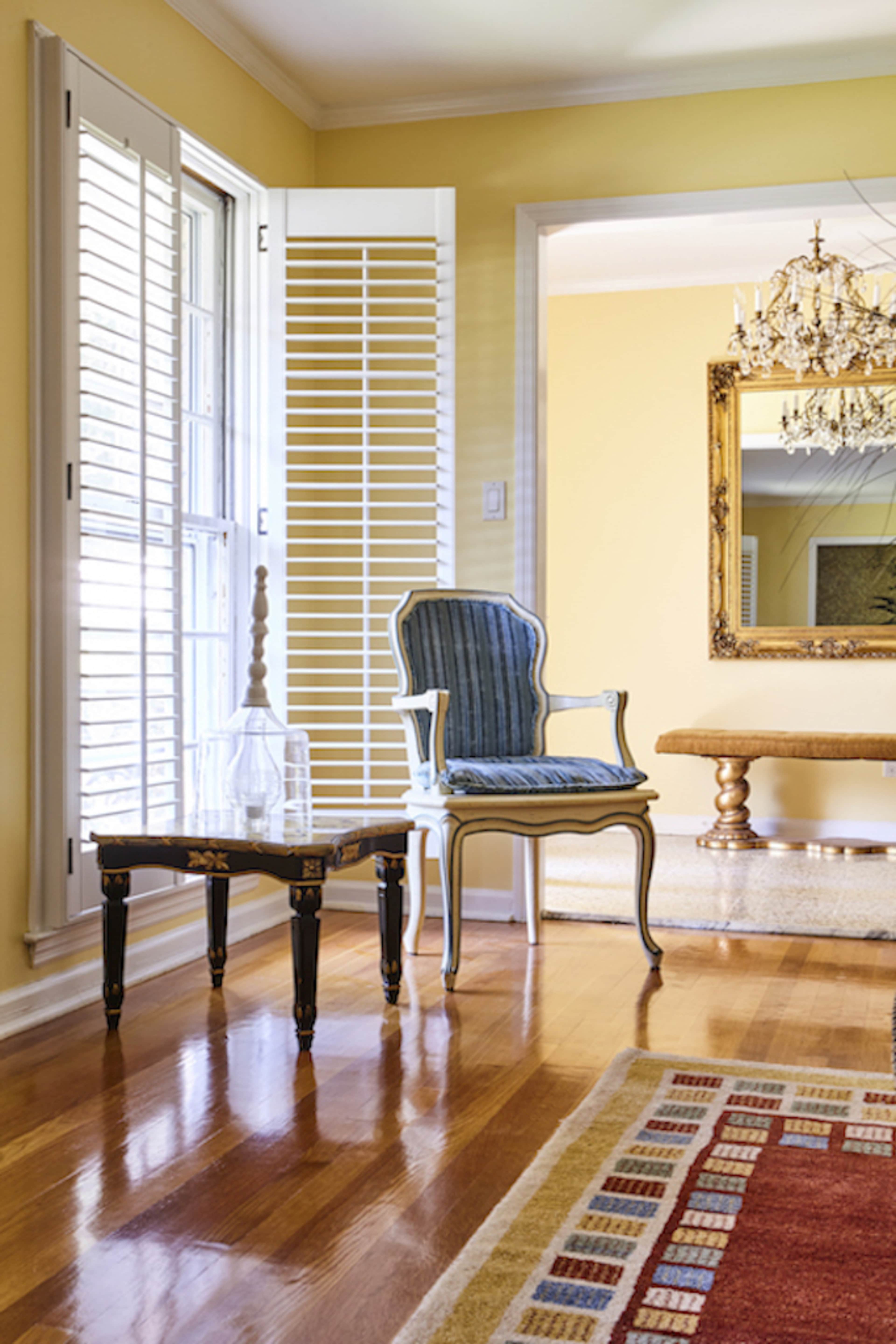 A blue and white striped chair sits beside a small black table in a brightly lit room with yellow walls and wooden floors.