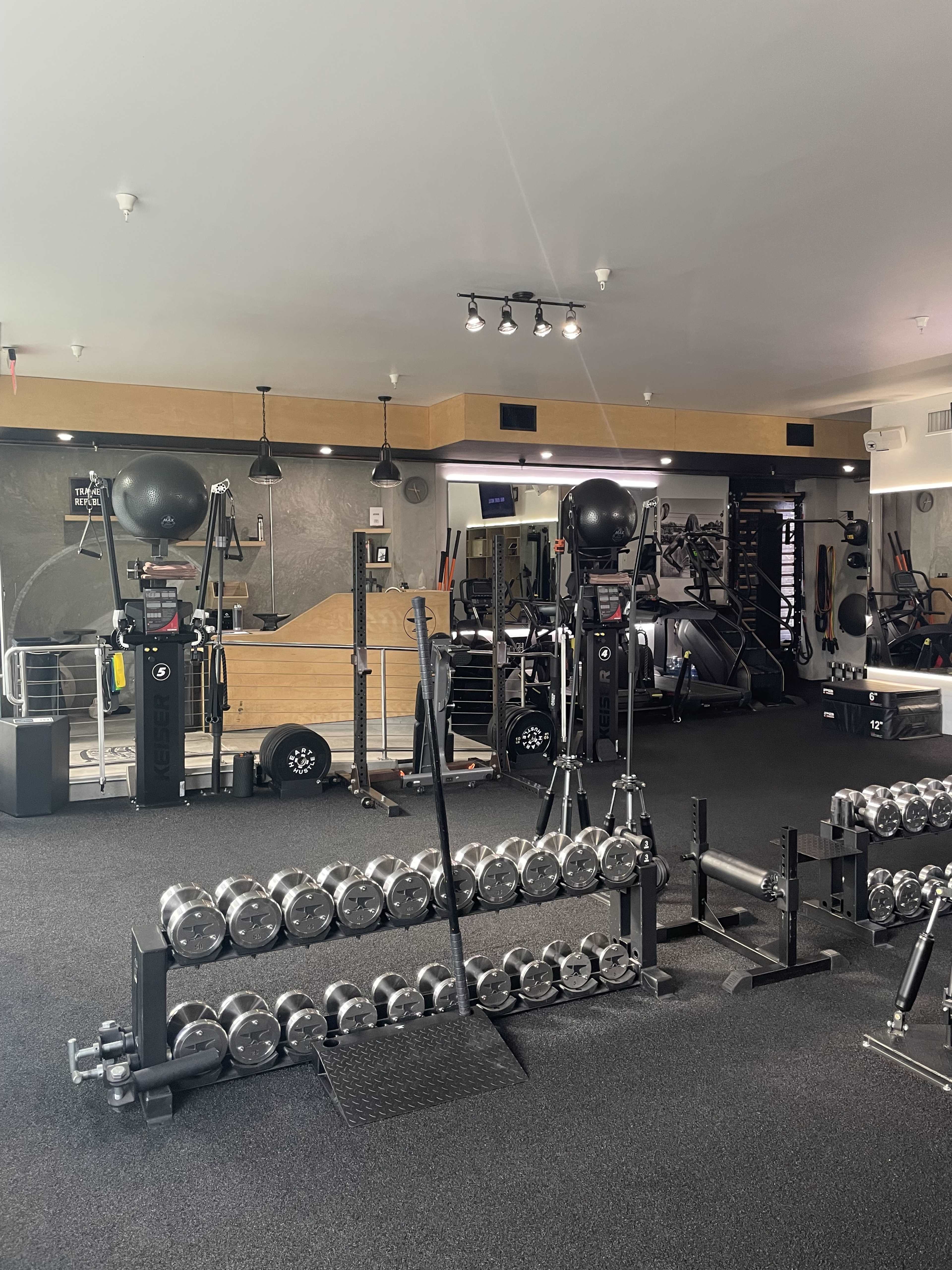 A well-equipped gym with a rack of dumbbells in the foreground and various exercise machines and equipment in the background.