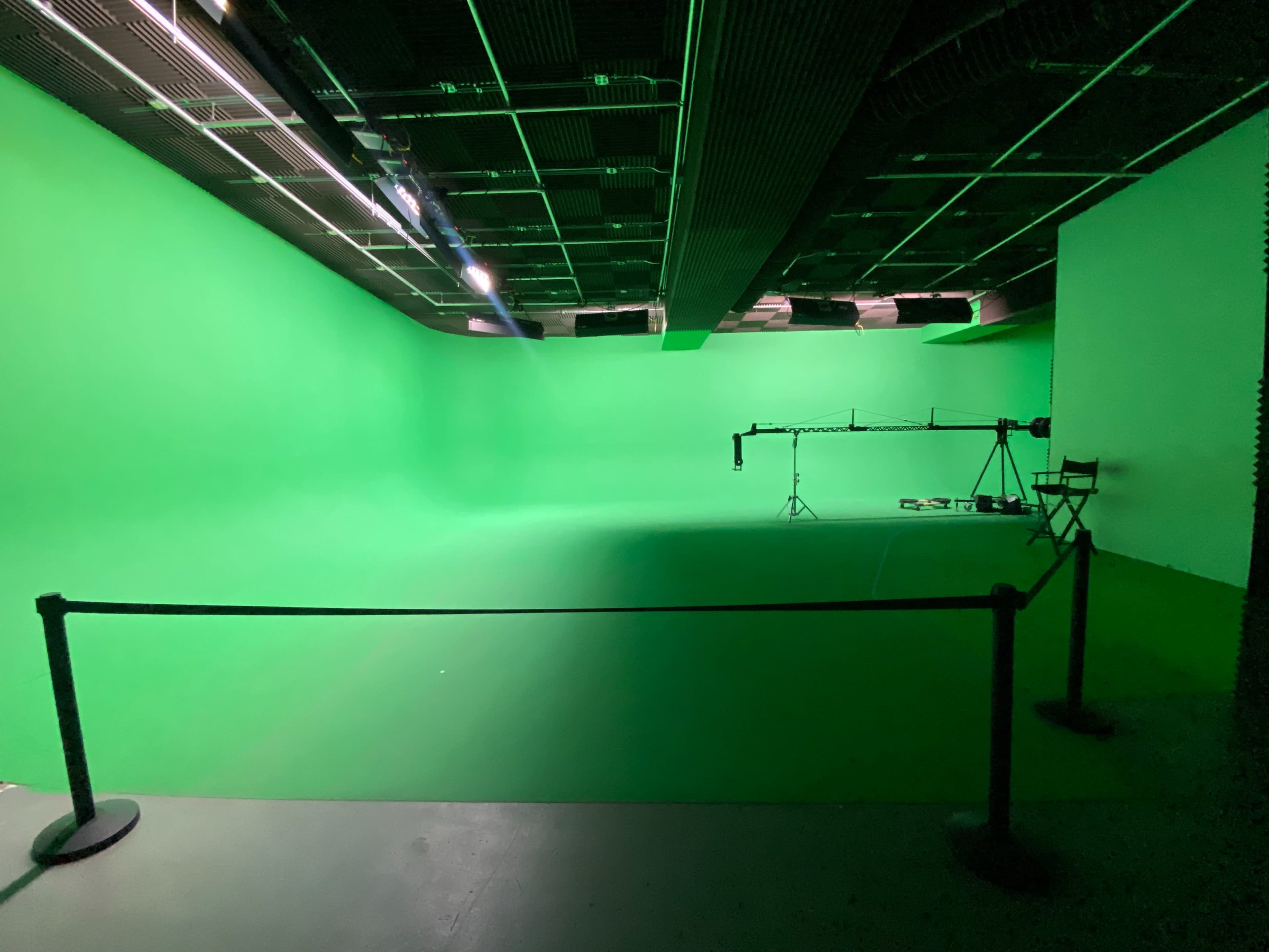 An empty green screen studio with adjustable lighting and a camera setup in the background.