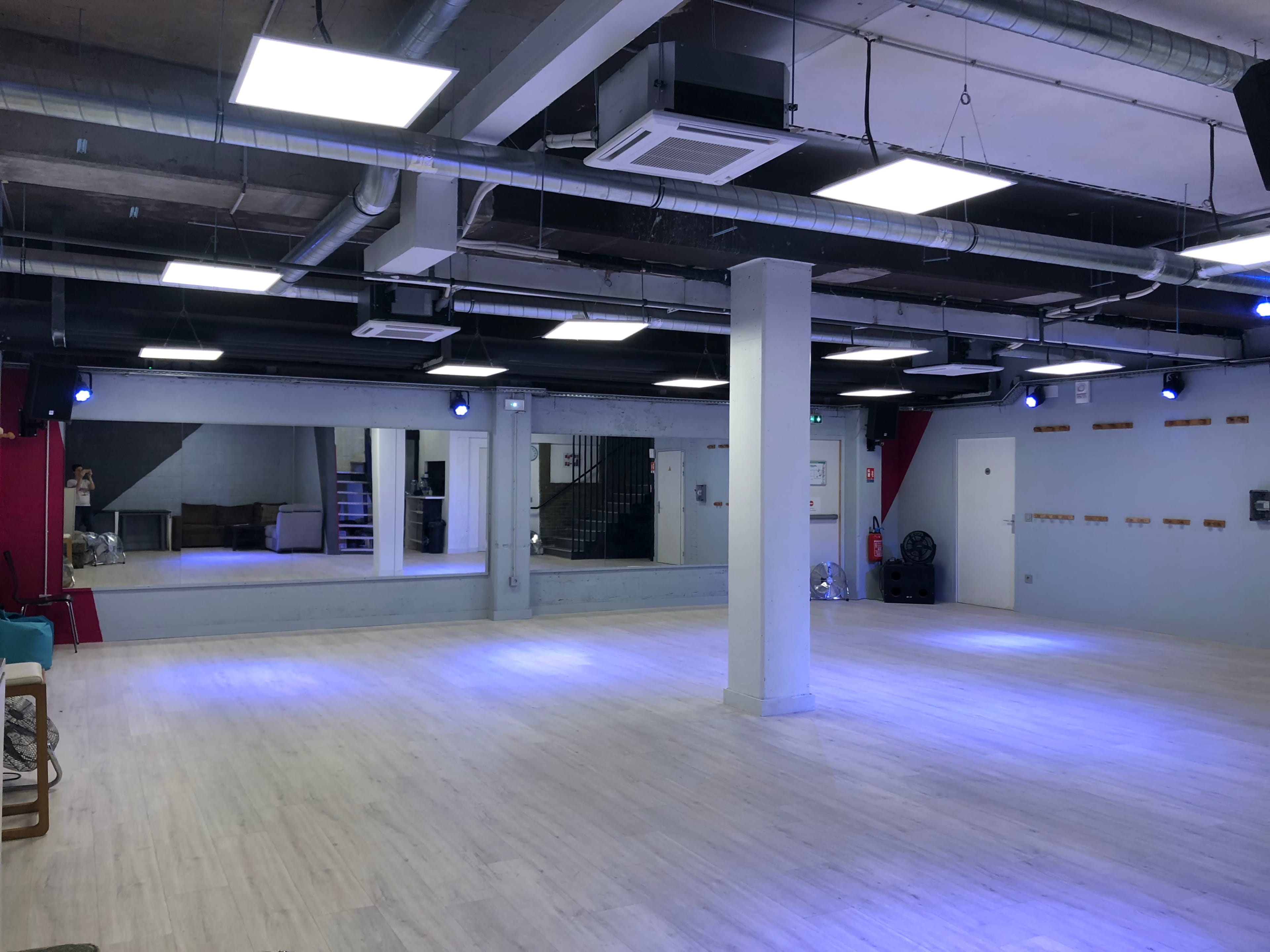 A spacious dance studio with wood flooring, bright ceiling lights, and large mirrors along one wall.