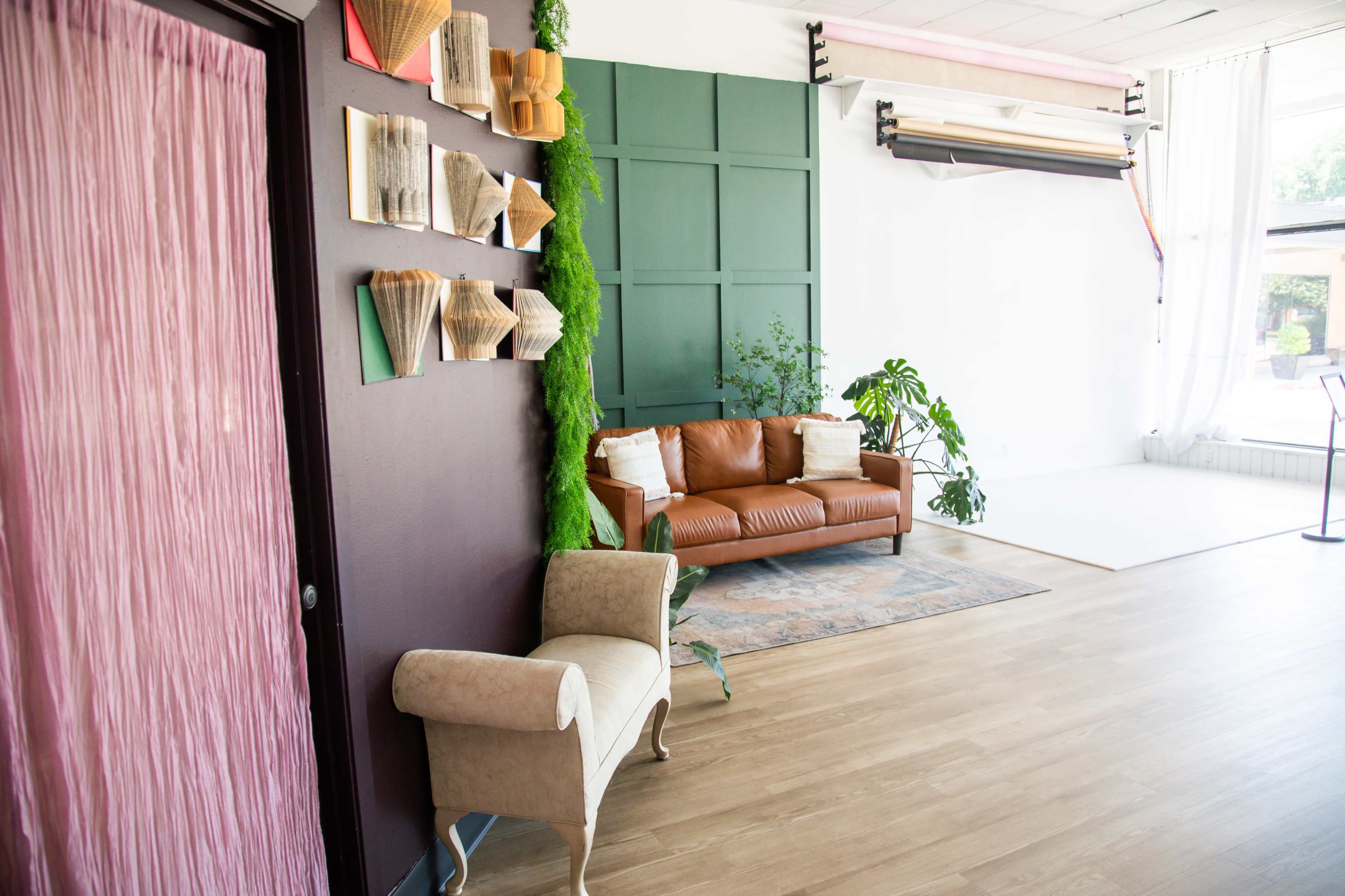 The image shows a modern interior space featuring a brown leather sofa, a decorative wall with paper art, and greenery against a backdrop of dark green panels.