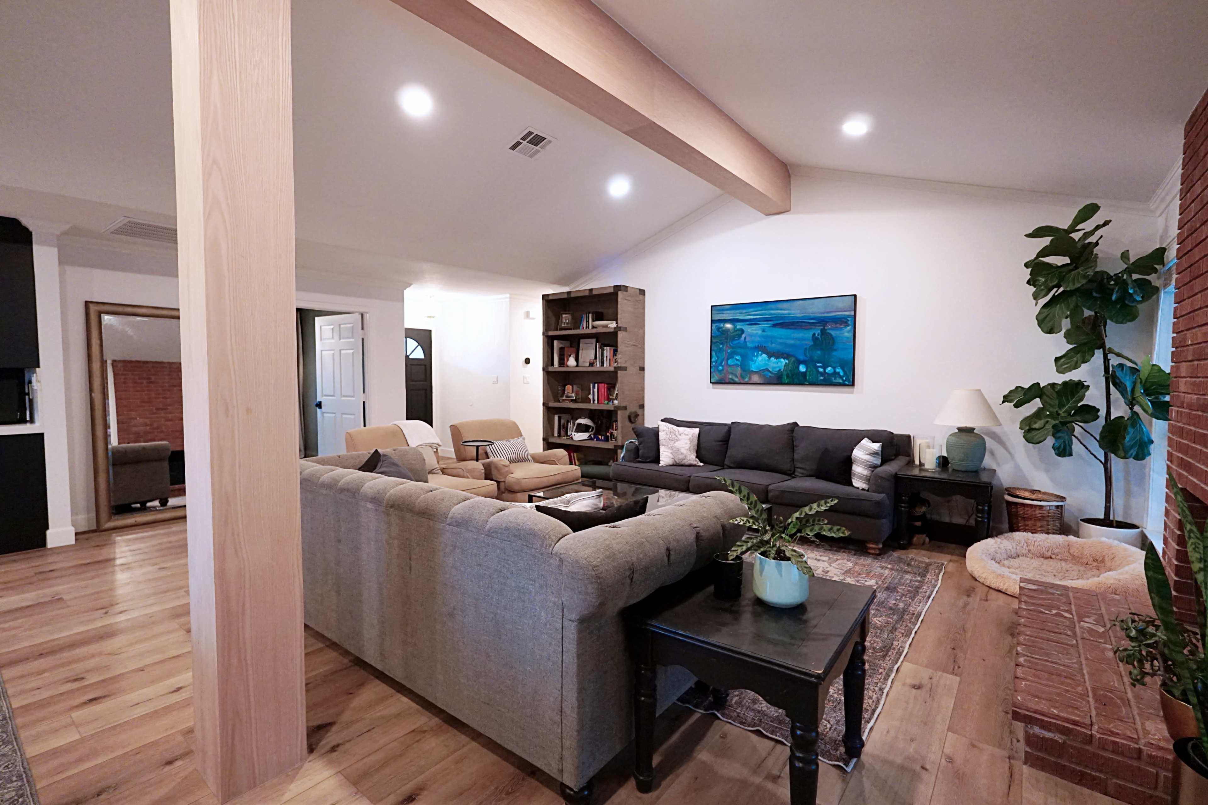 The living room features a comfortable seating arrangement with a sofa, armchairs, a coffee table, and a bookshelf, set against a backdrop of wood accents and a brick wall.