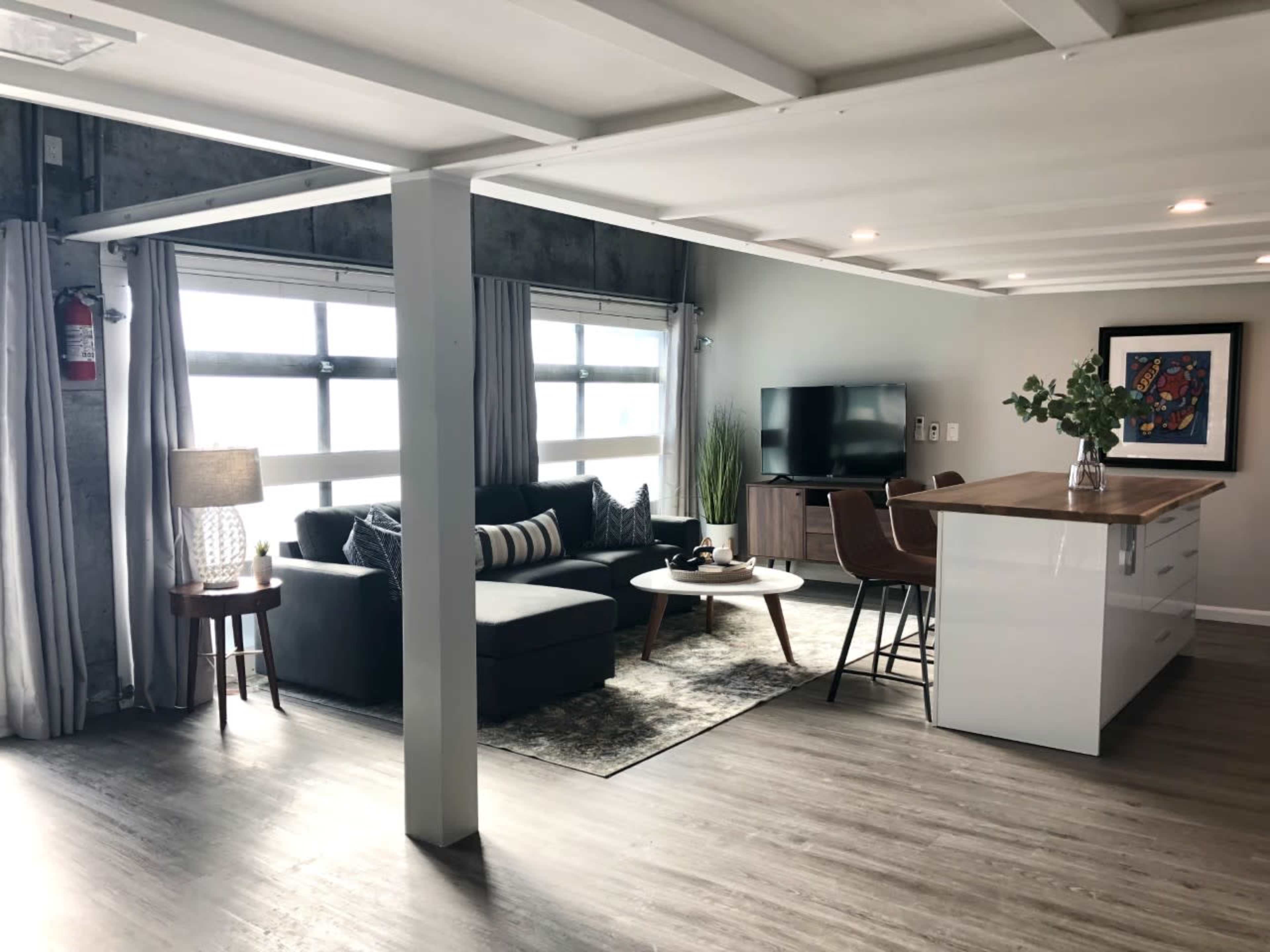 A modern open-concept living space featuring a sofa, coffee table, television, and kitchen island with seating.