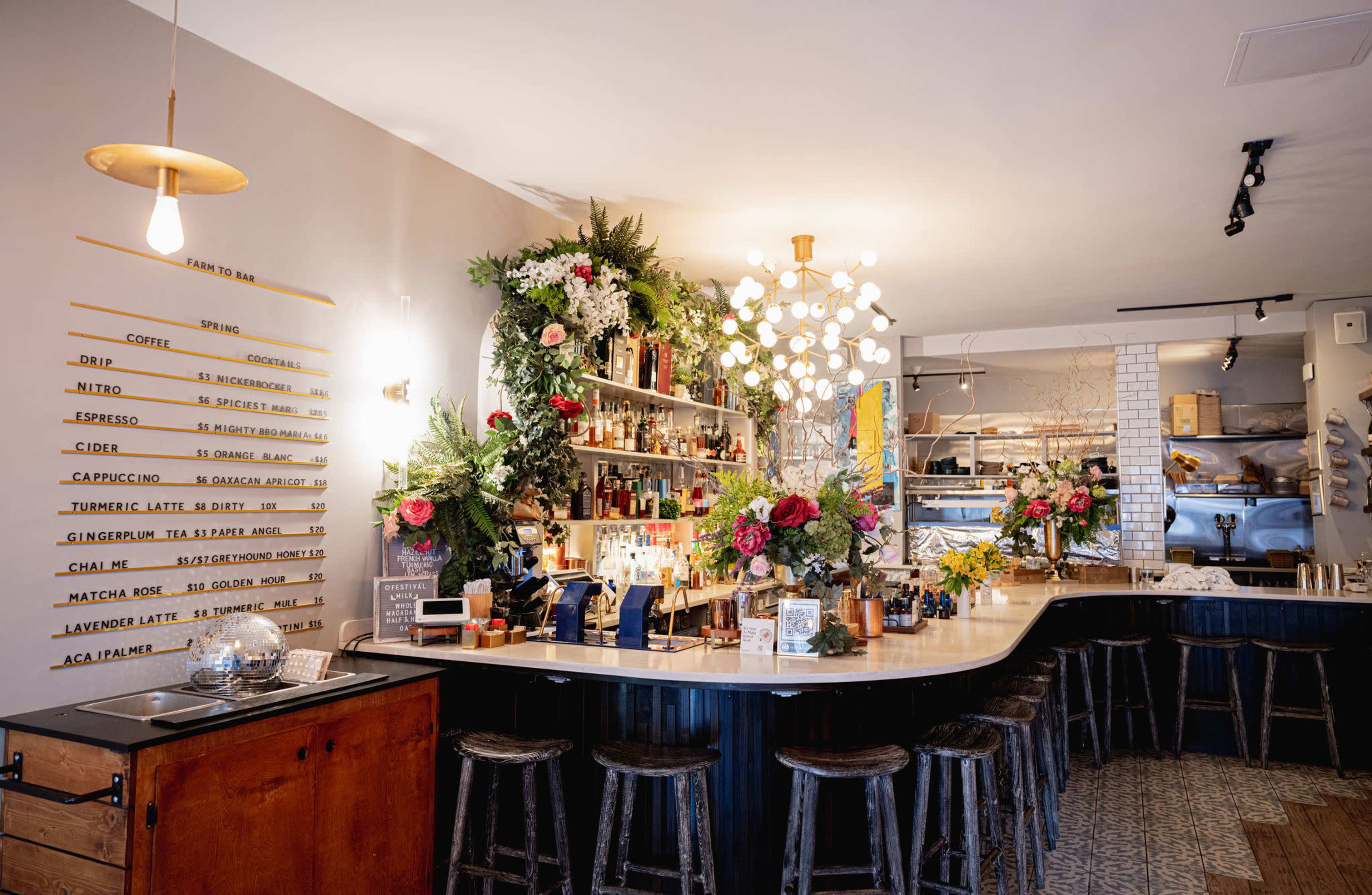 A stylish bar area with a curved counter, decorated with various bottles and vibrant floral arrangements.