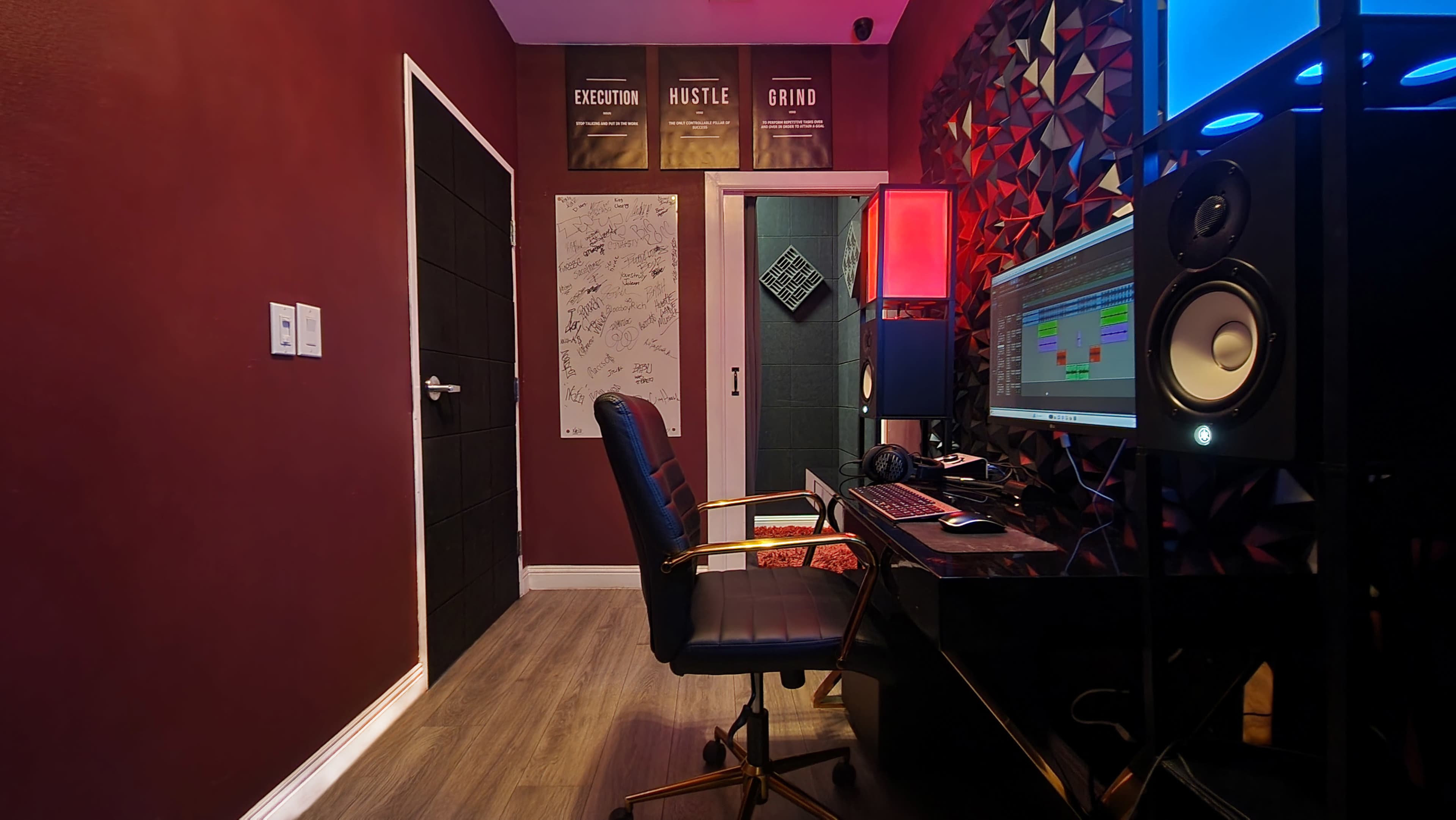 A small recording studio with a computer desk, a black office chair, and colorful wall decorations.