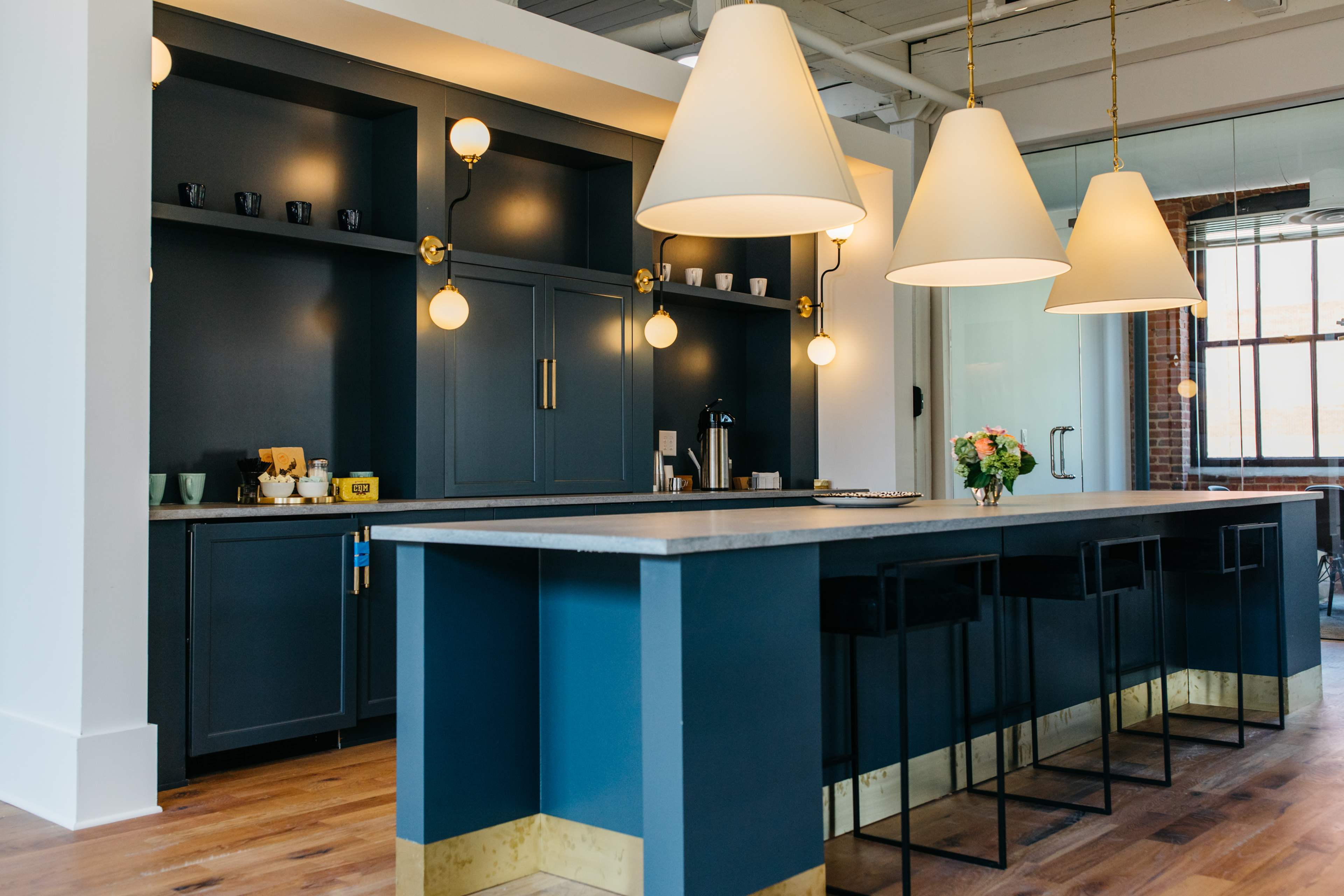 A modern kitchen features a long island with bar stools, a blue cabinetry backdrop, and large pendant lights.