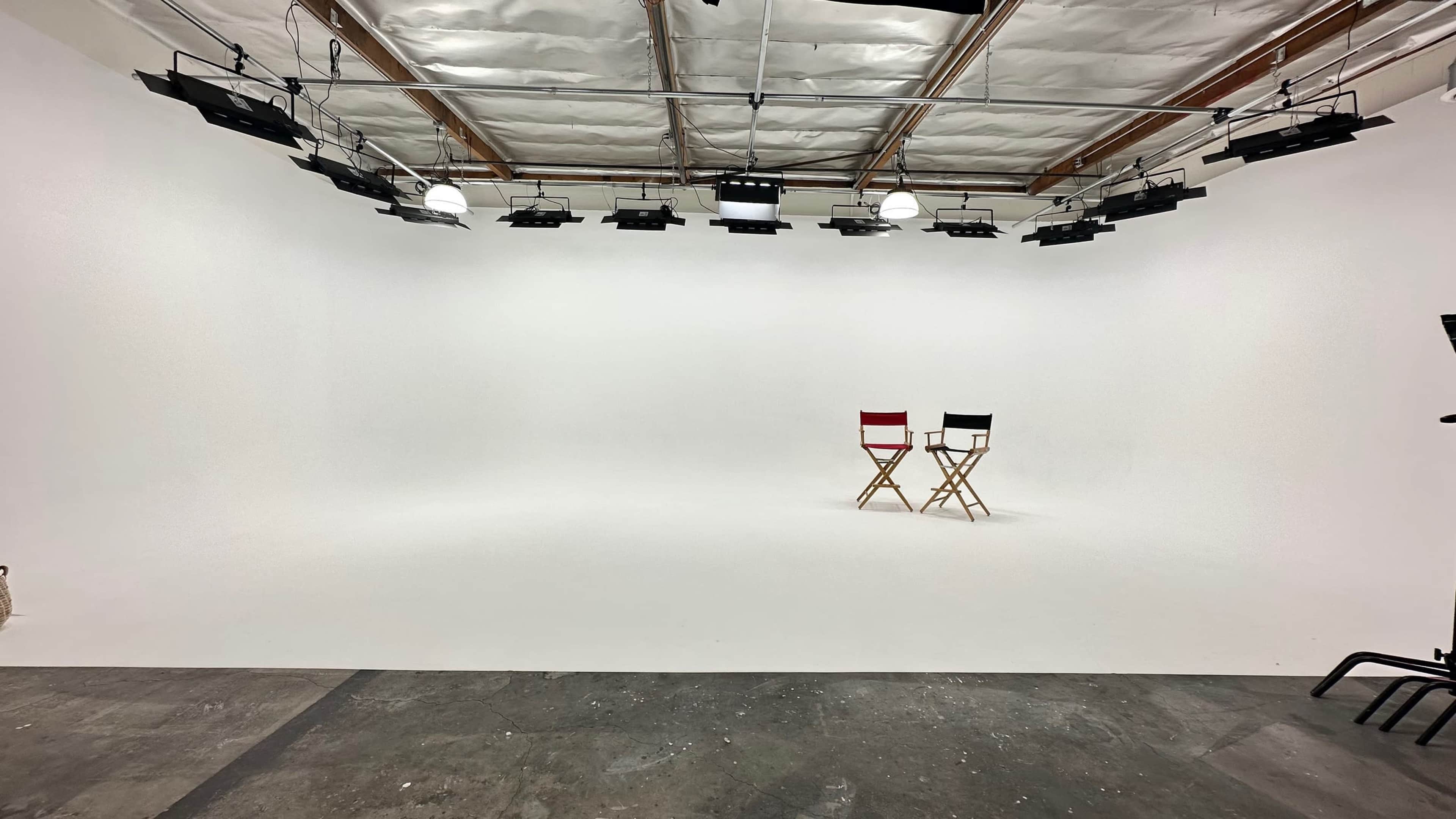A blank studio space with two director's chairs, one red and one black, positioned on a white backdrop.