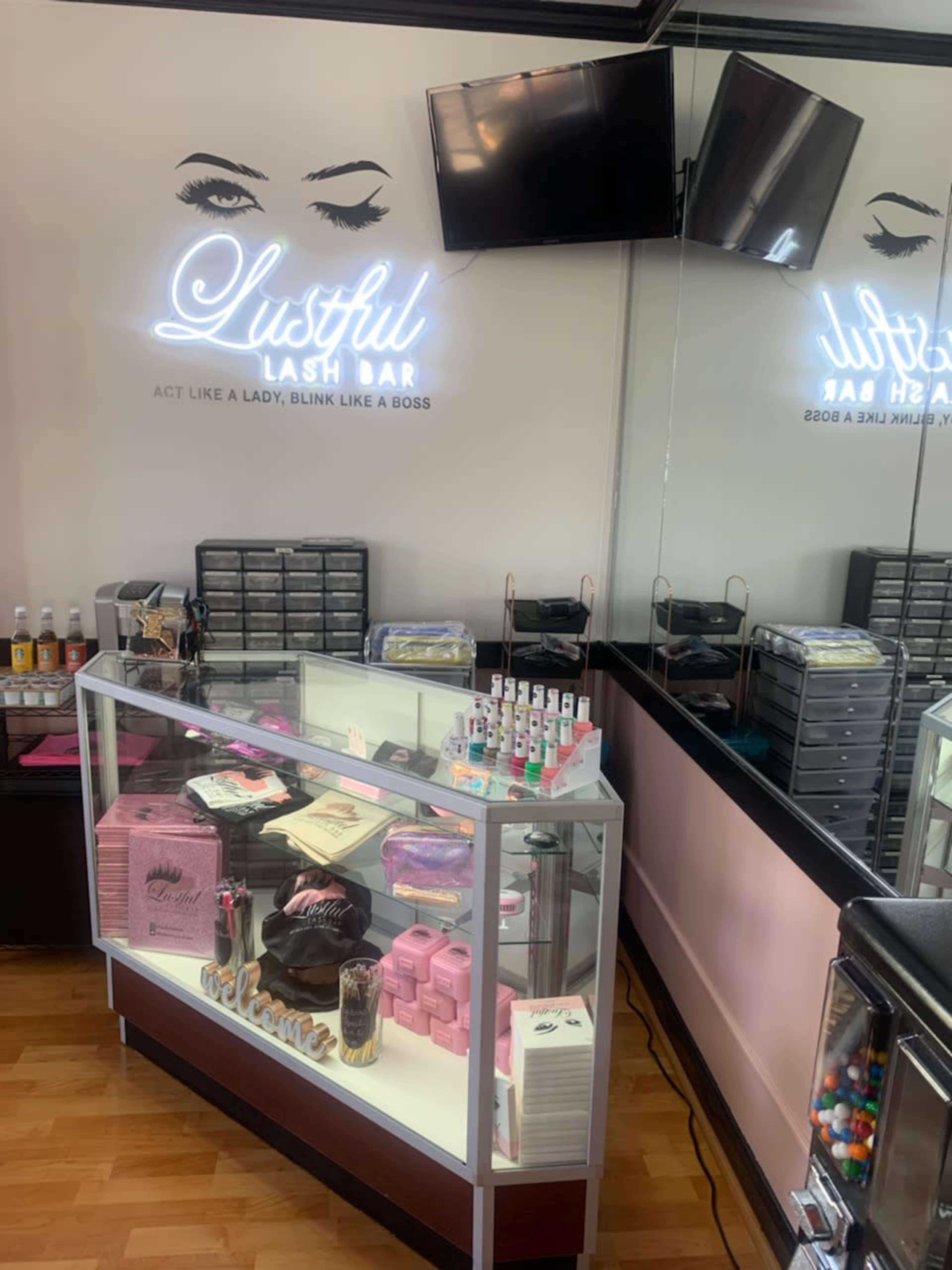 The image shows a beauty salon display with products and a sign that reads "Lustful Lash Bar" along with a mirror reflecting the interior.