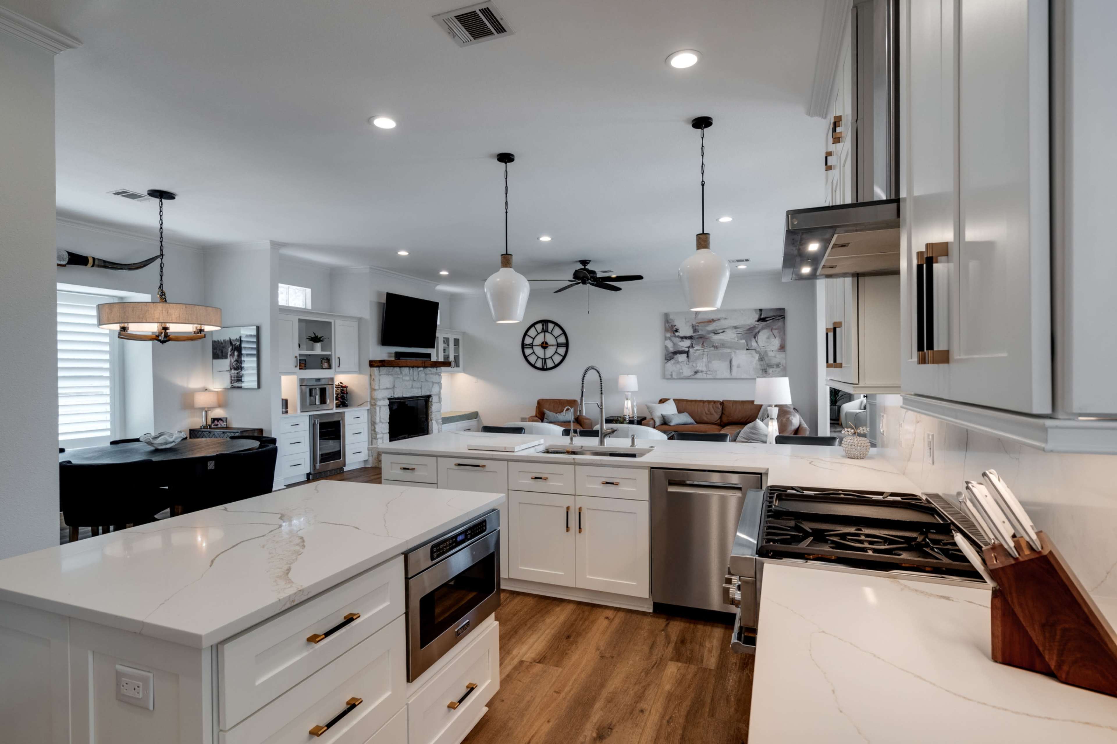 A modern kitchen features white cabinetry, stainless steel appliances, and an island with a marble countertop, opening up to a cozy living area.