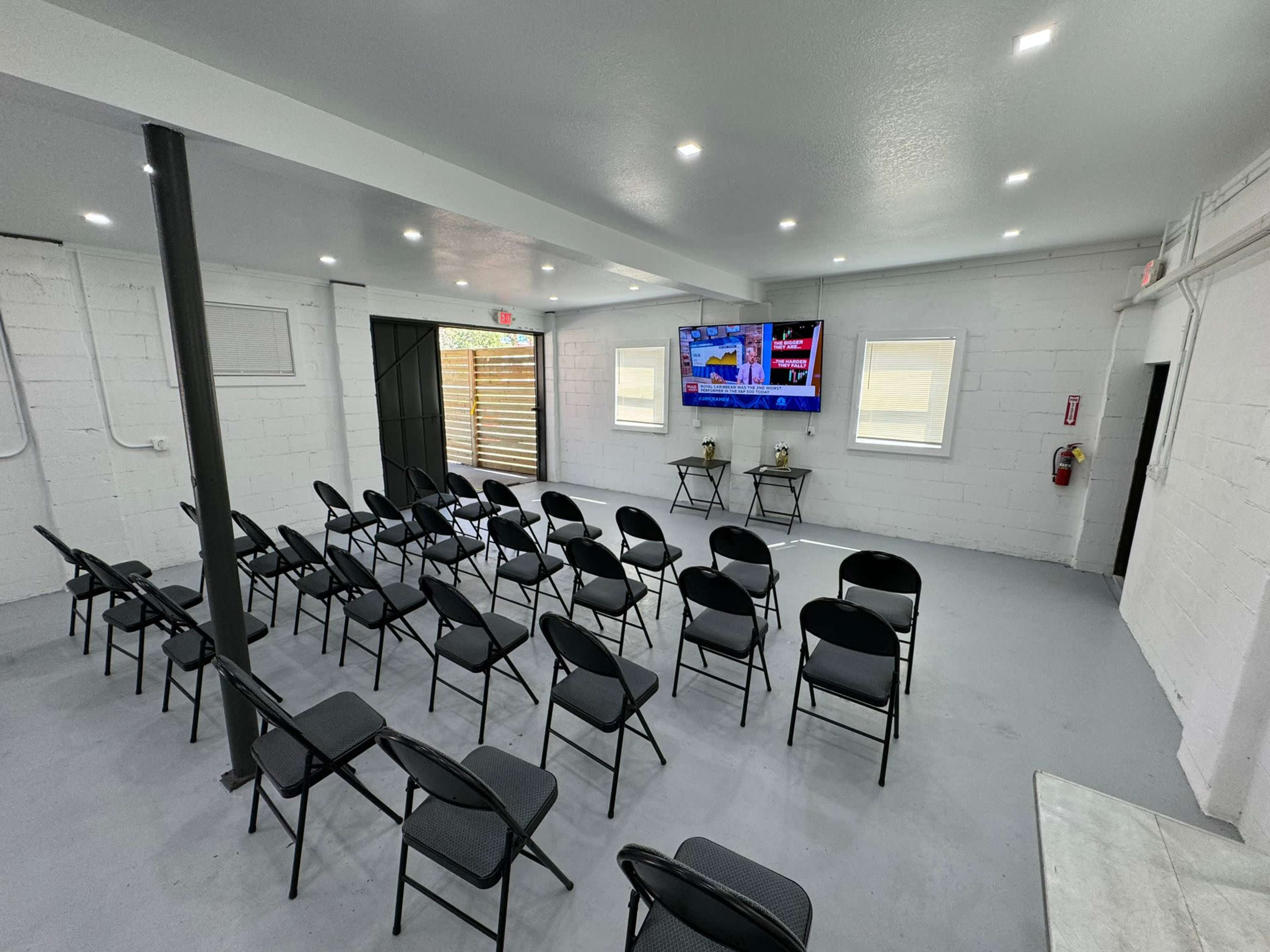A neatly arranged meeting room with black folding chairs facing two large screens mounted on a white wall.