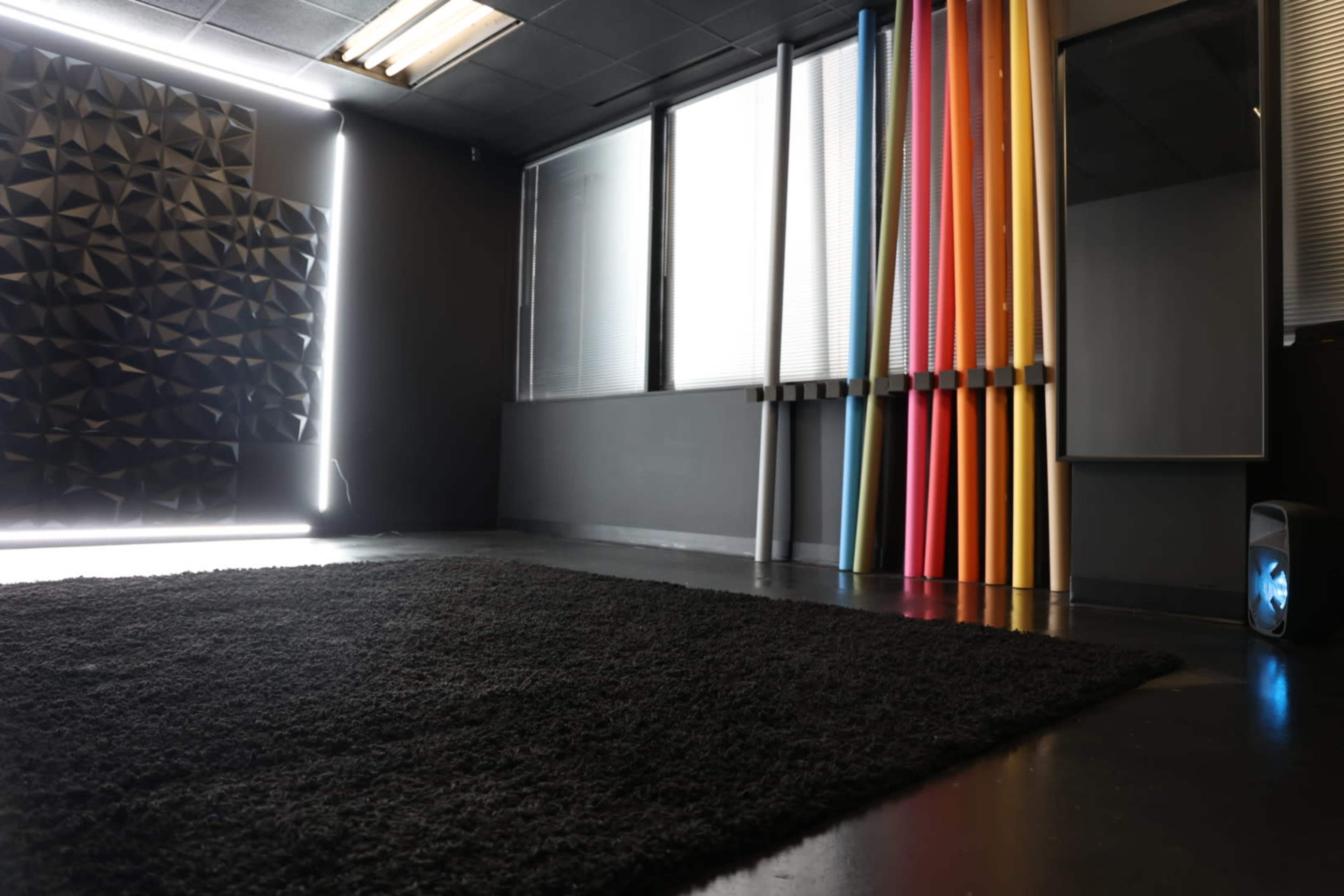 A modern room with a black carpet, textured walls, and colorful cylindrical panels arranged vertically against a dark background.