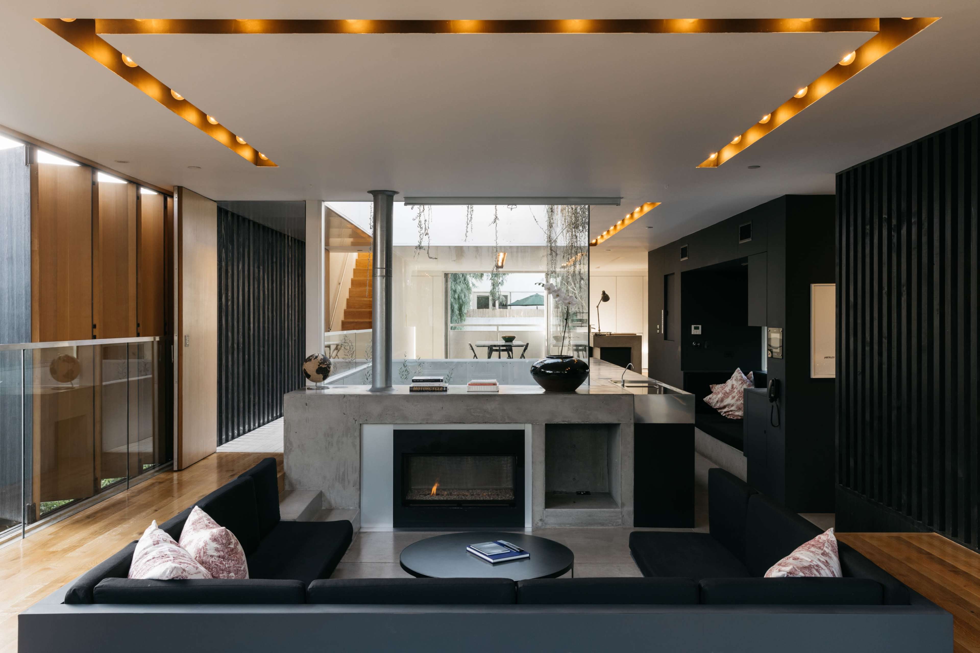 A modern living room featuring a concrete fireplace, black sofas, and large windows allowing natural light to enter.