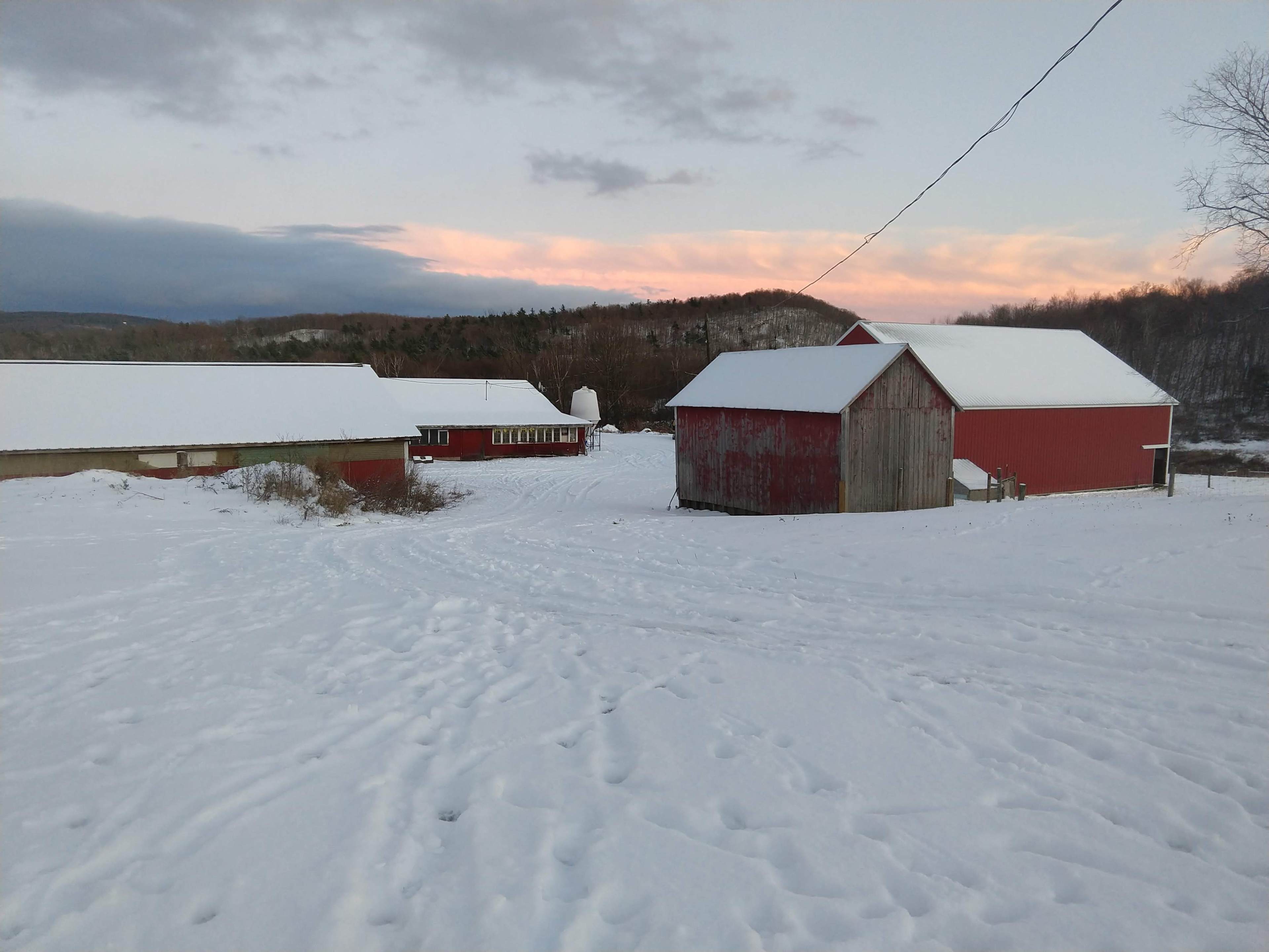 A snowy landscape features red barns set against a backdrop of hills and a pastel sky at dusk.