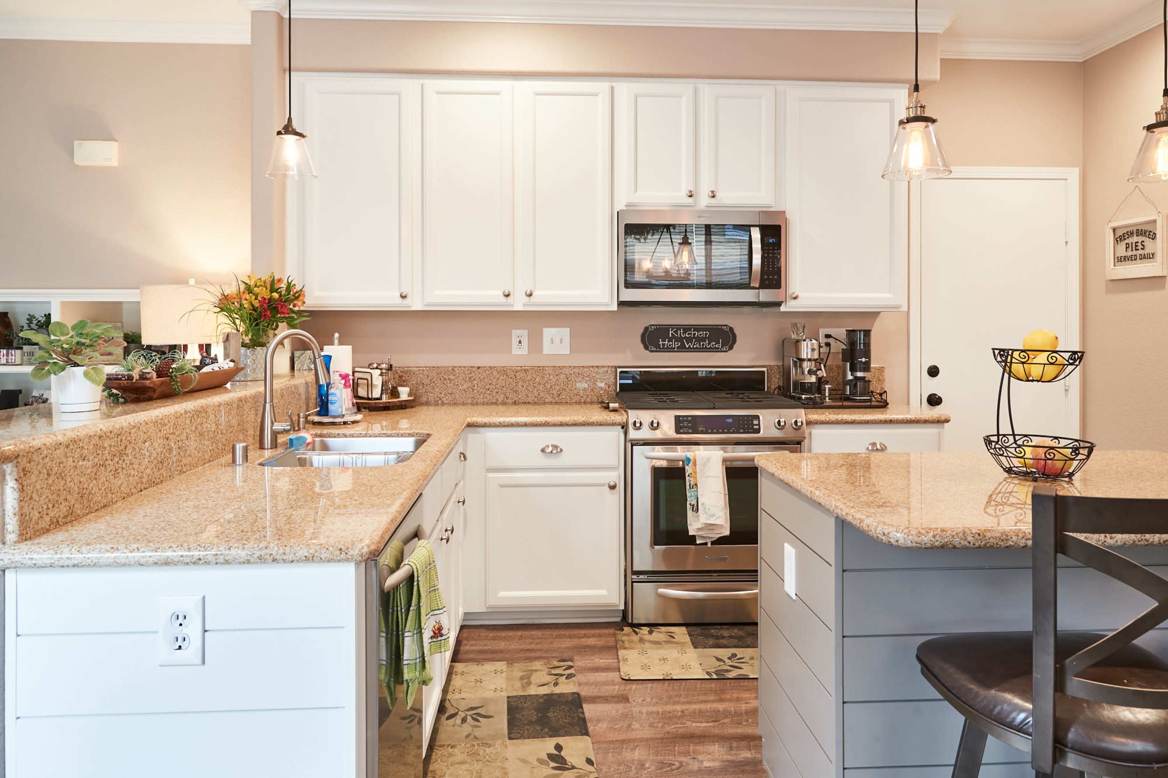 A modern kitchen features white cabinets, granite countertops, a stainless steel stove, and pendant lighting.