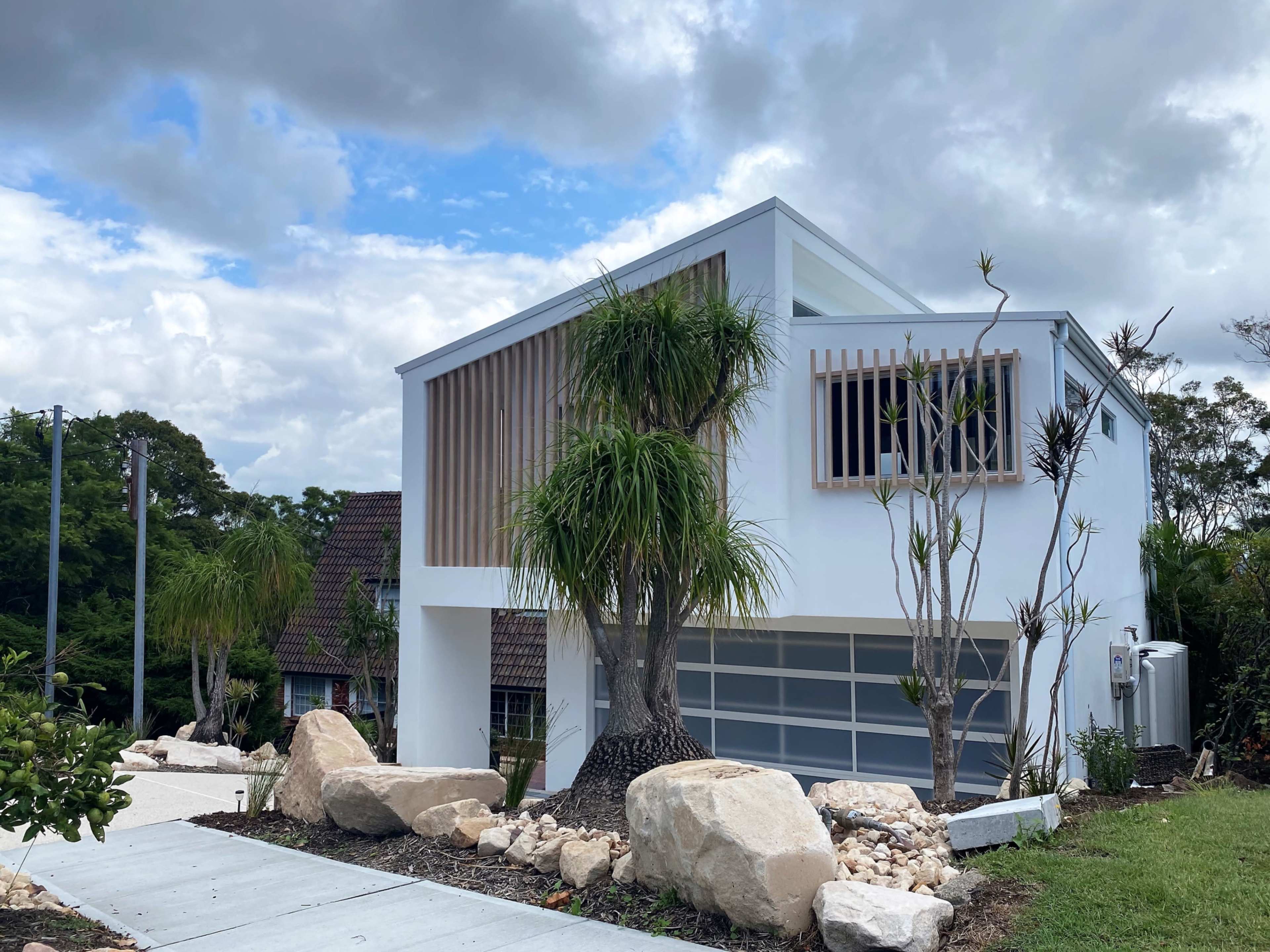 A modern, two-story house with wooden slat accents, surrounded by landscaped stones and plants.