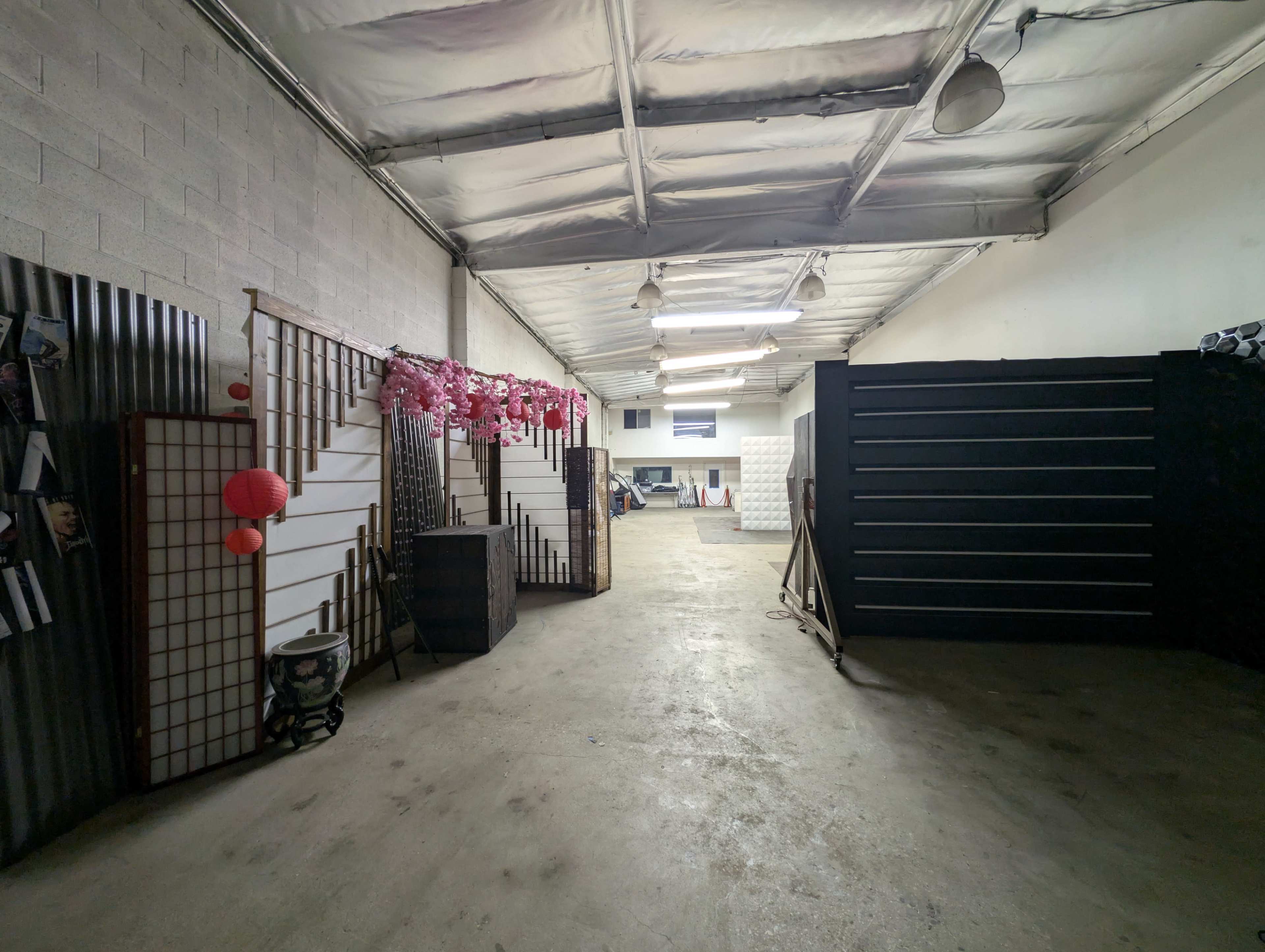 The image depicts a long, narrow storage or workspace area featuring dividing walls, decorative lanterns, and several items along the sides.