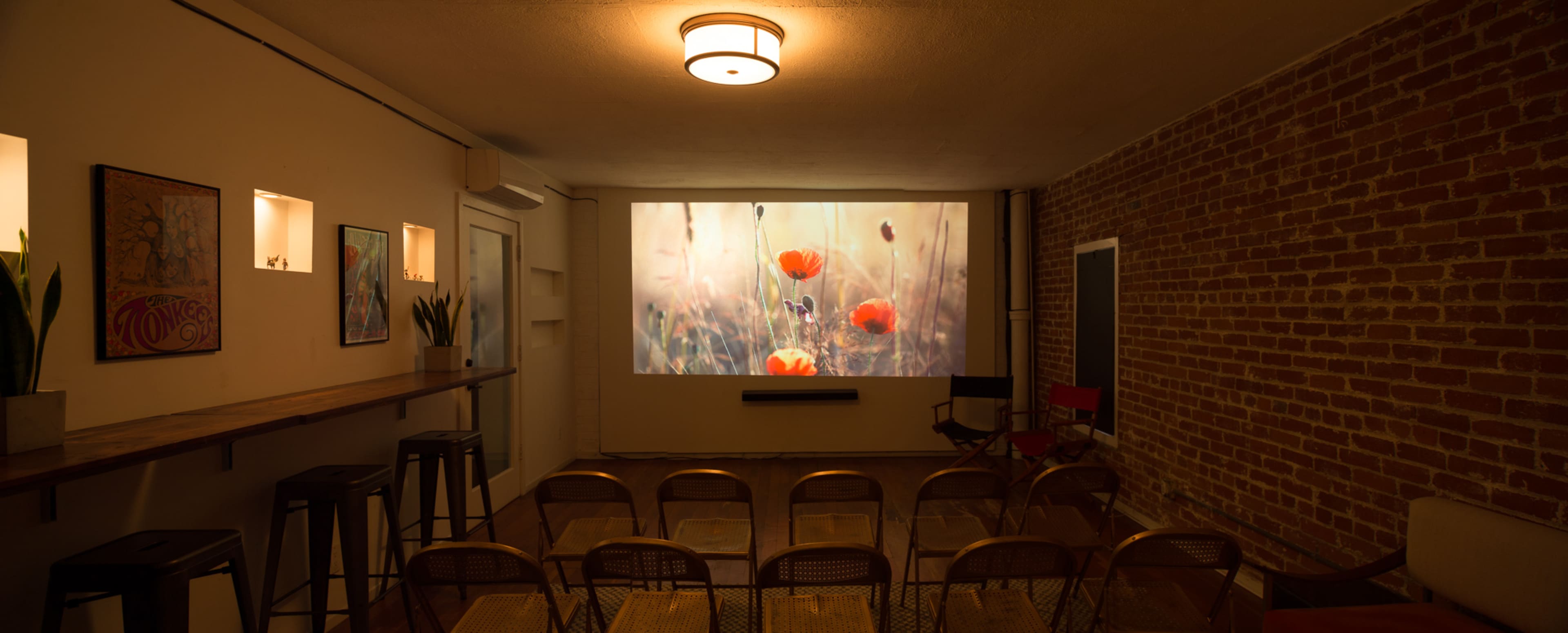 A cozy room with brick walls, featuring rows of chairs facing a projection of flowers on a large screen.