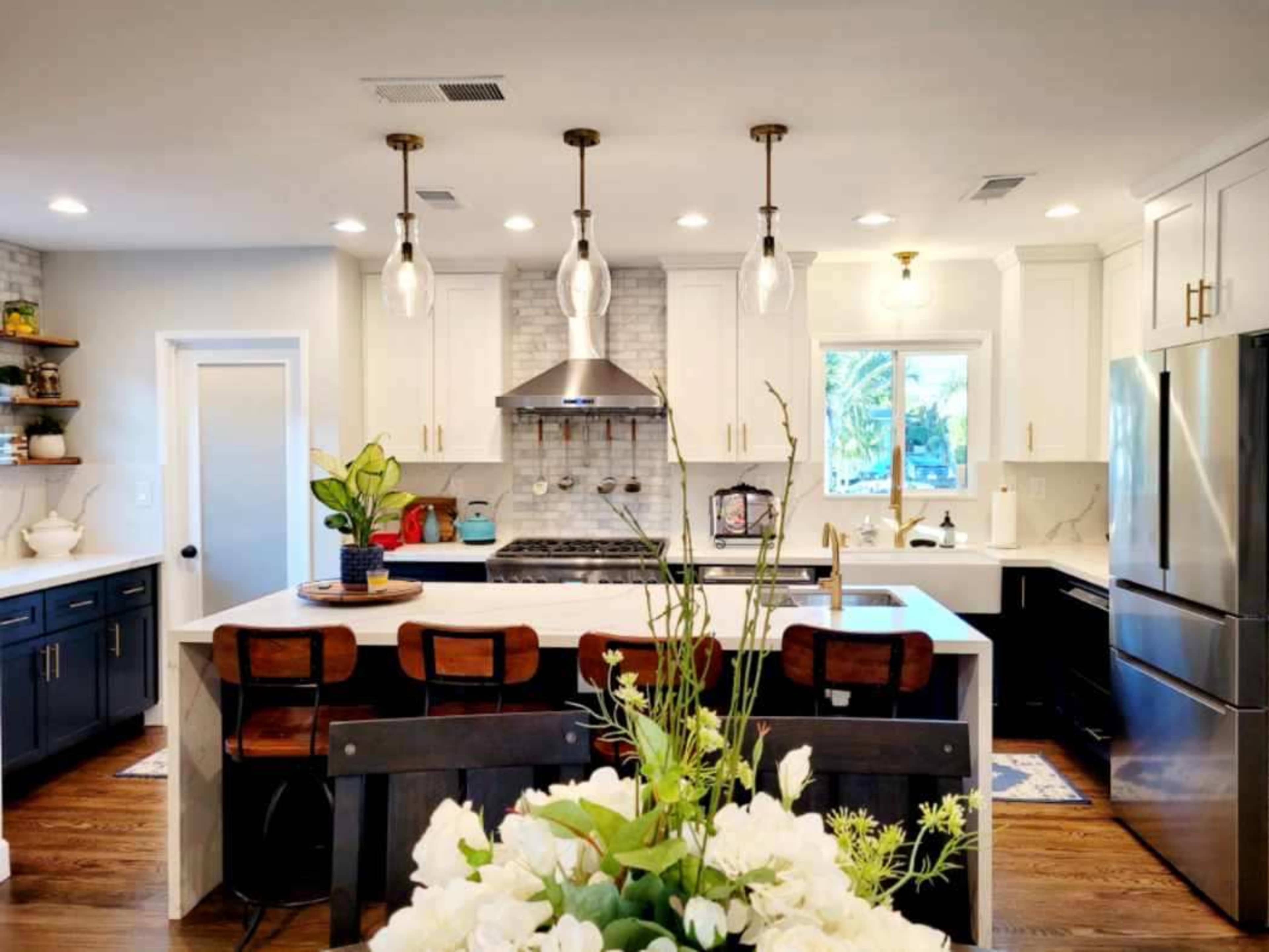 A modern kitchen featuring white cabinets, a central island with seating, stainless steel appliances, and decorative lighting fixtures.