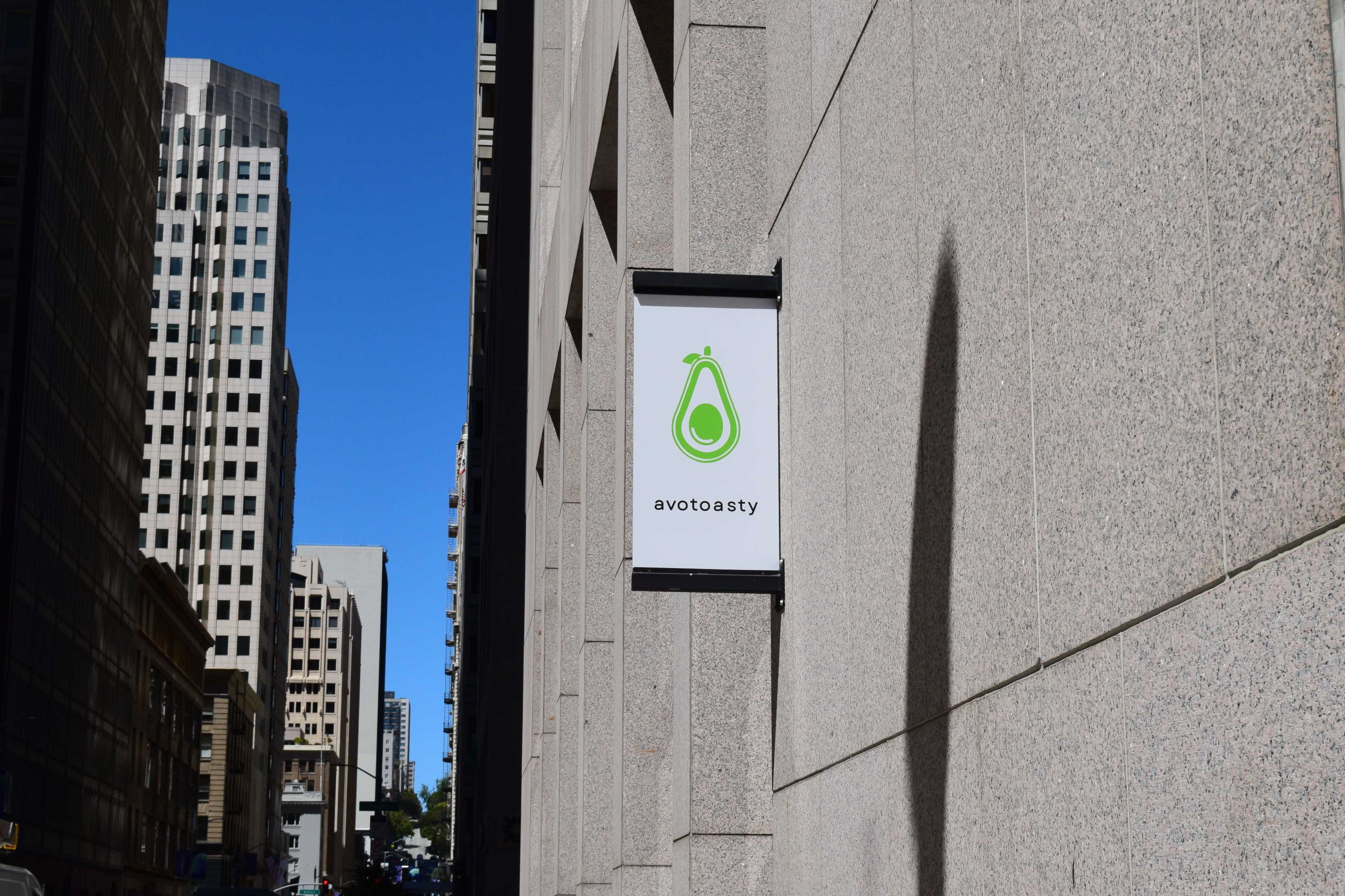 The image shows a building facade with a sign displaying the logo and name "avtotasty," featuring an avocado graphic.
