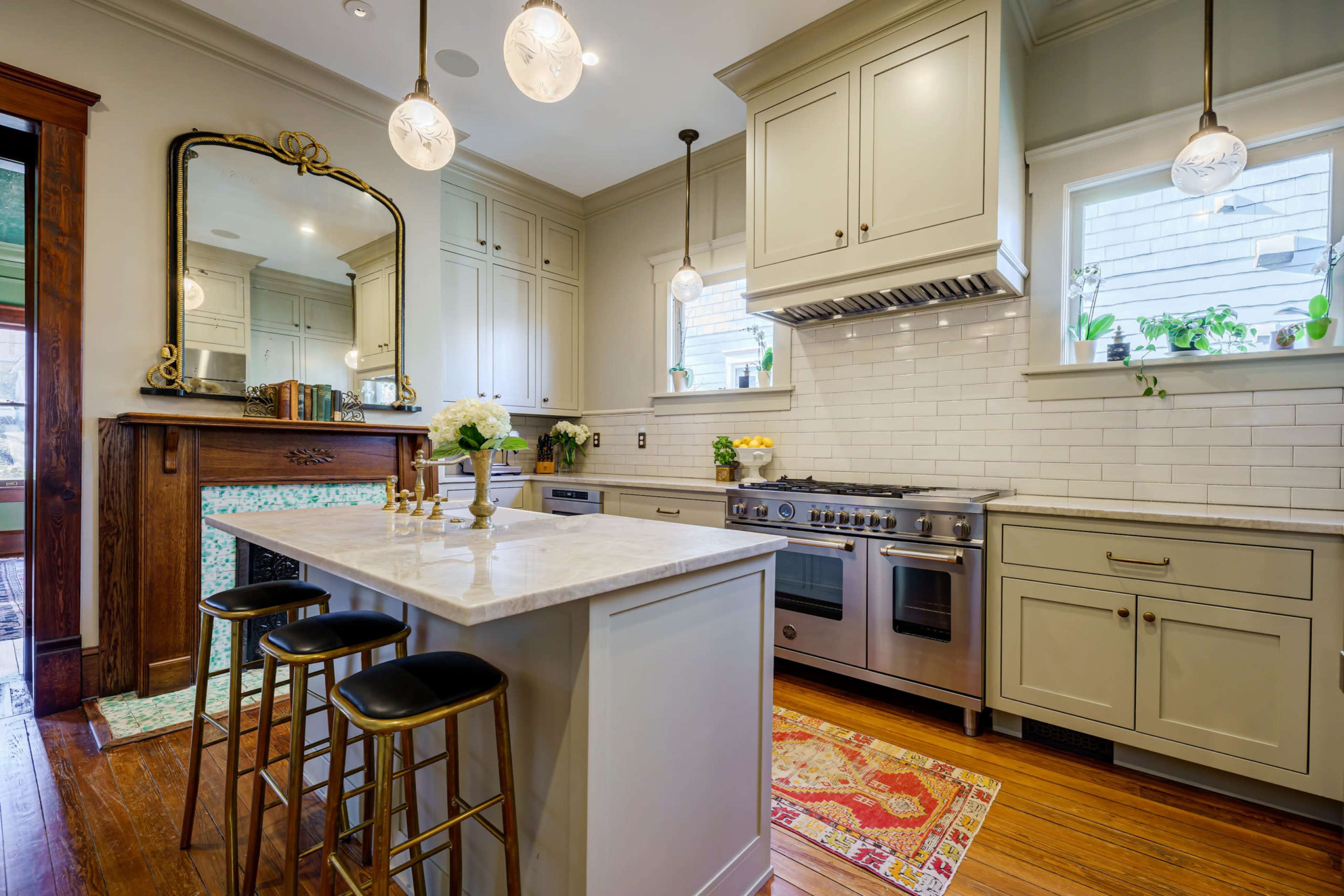 A modern kitchen with white cabinetry, stainless steel appliances, a large island with three bar stools, and decorative lighting fixtures.