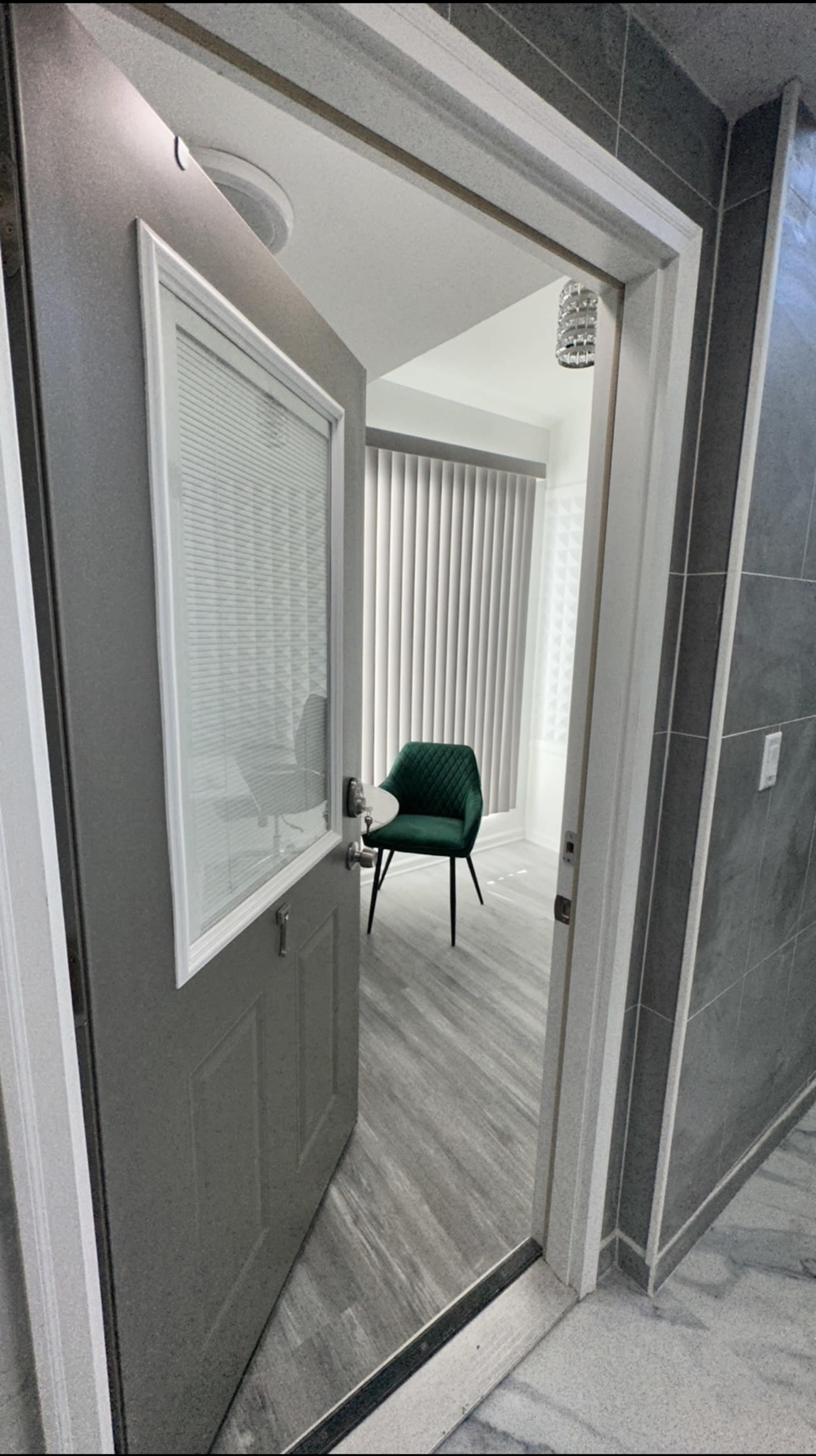 A green chair is positioned in a well-lit room visible through an open door with a glass panel.