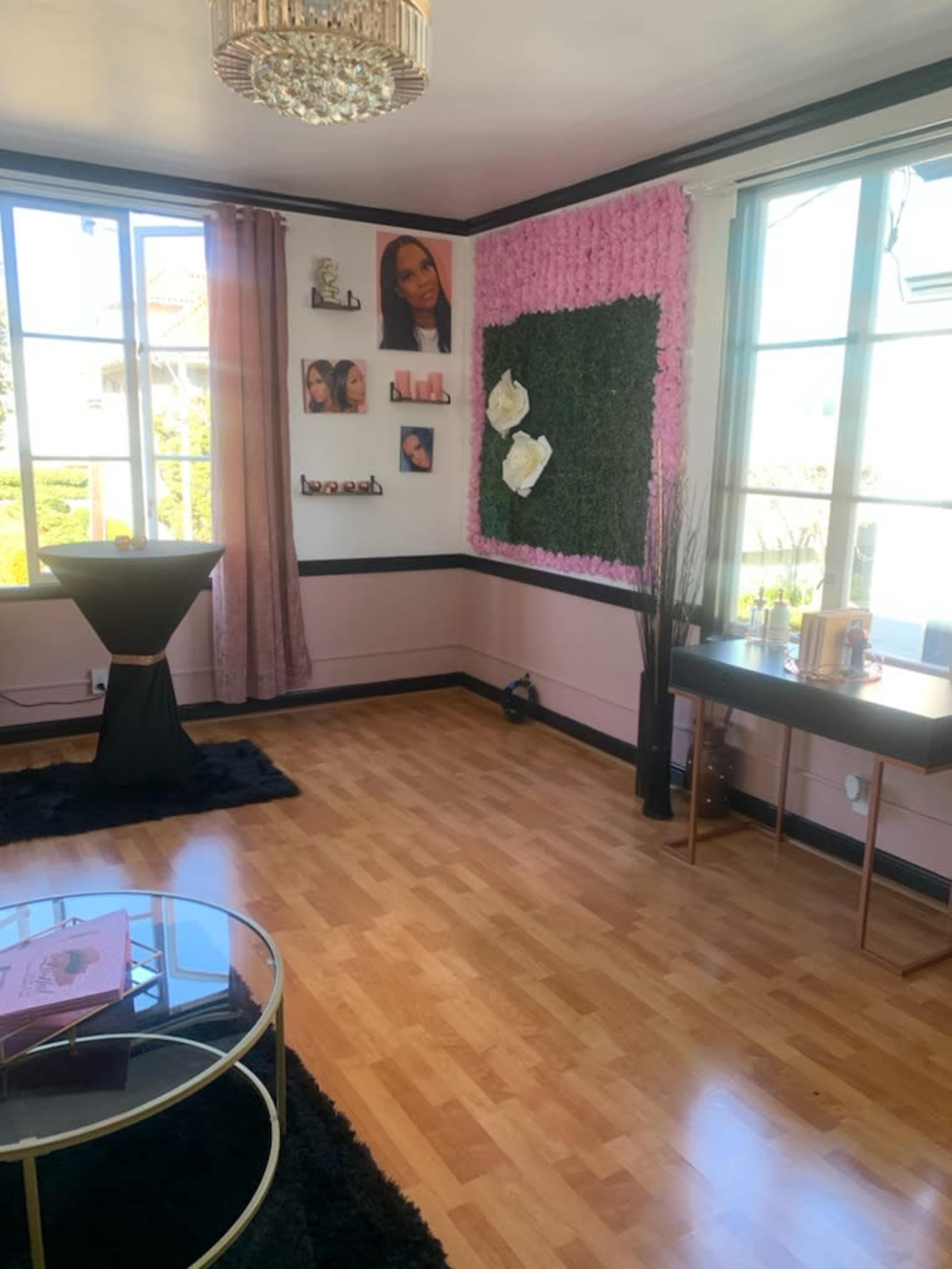 The image shows a well-lit room with large windows, featuring a black table, decorative wall art, a floral accent wall, and a coffee table.