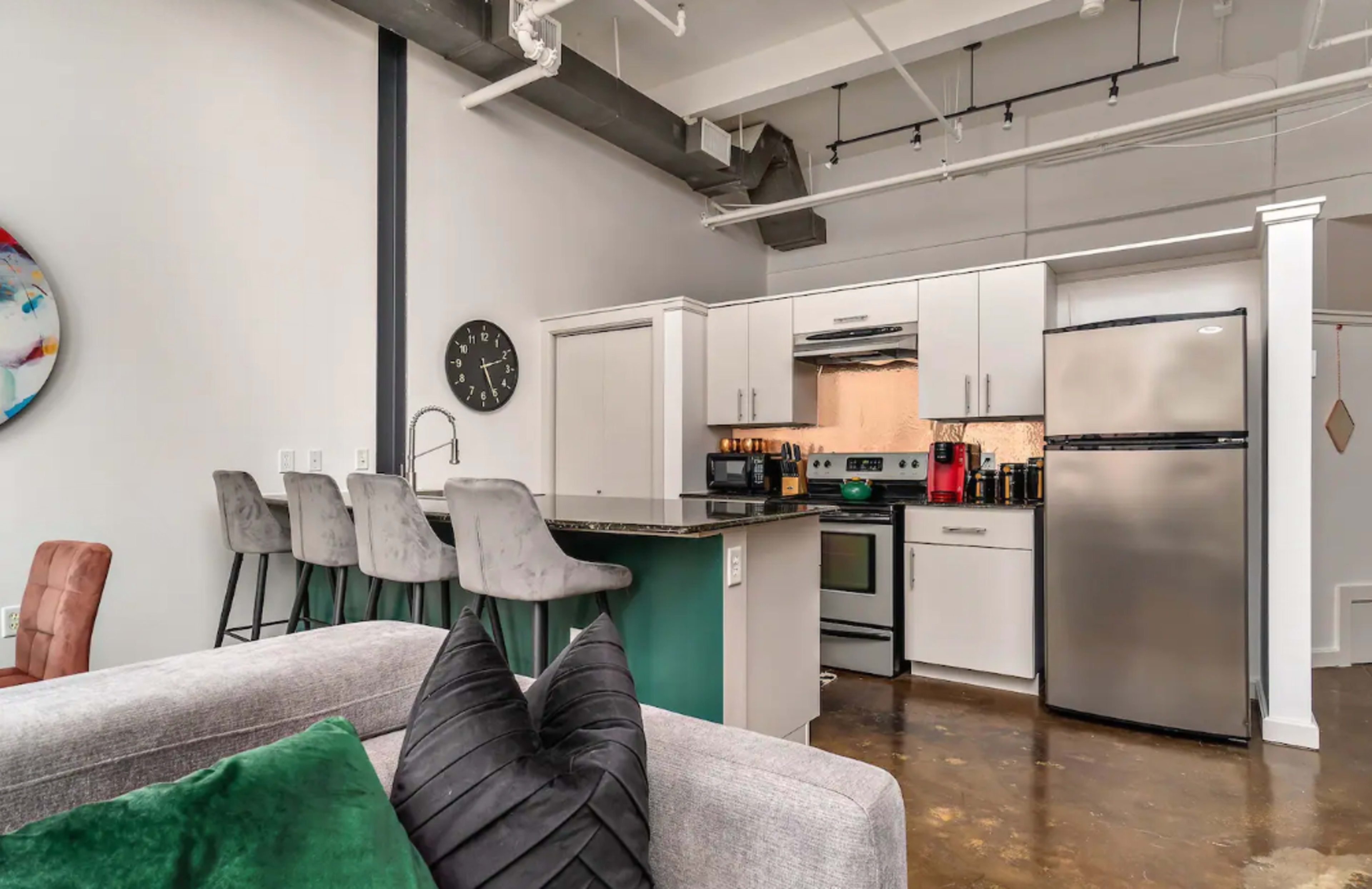 A modern kitchen with stainless steel appliances, a light-colored island with bar stools, and an open layout connecting to a living area.