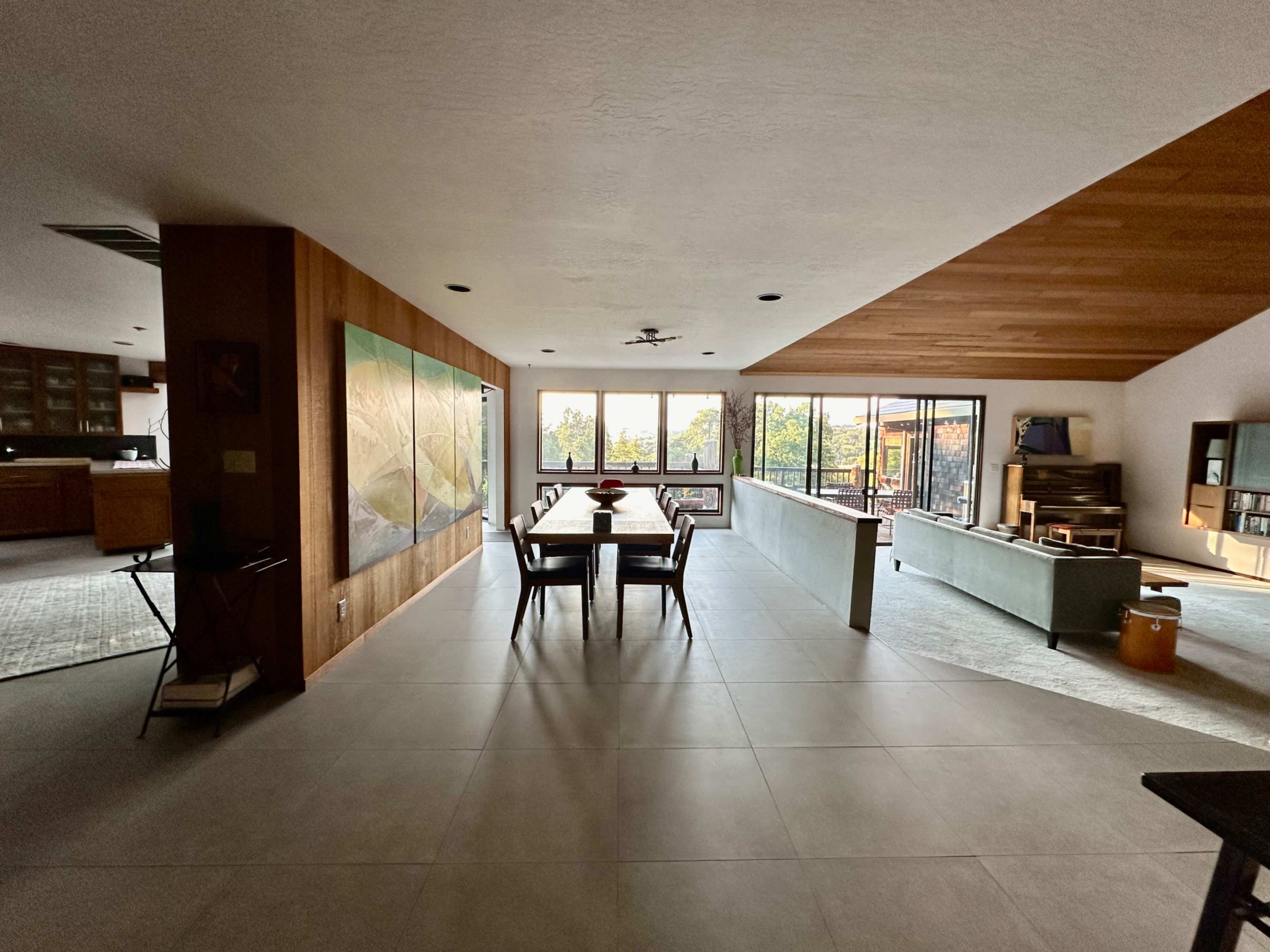 The image shows a spacious, modern living area with a dining table, large windows, and sleek furniture.