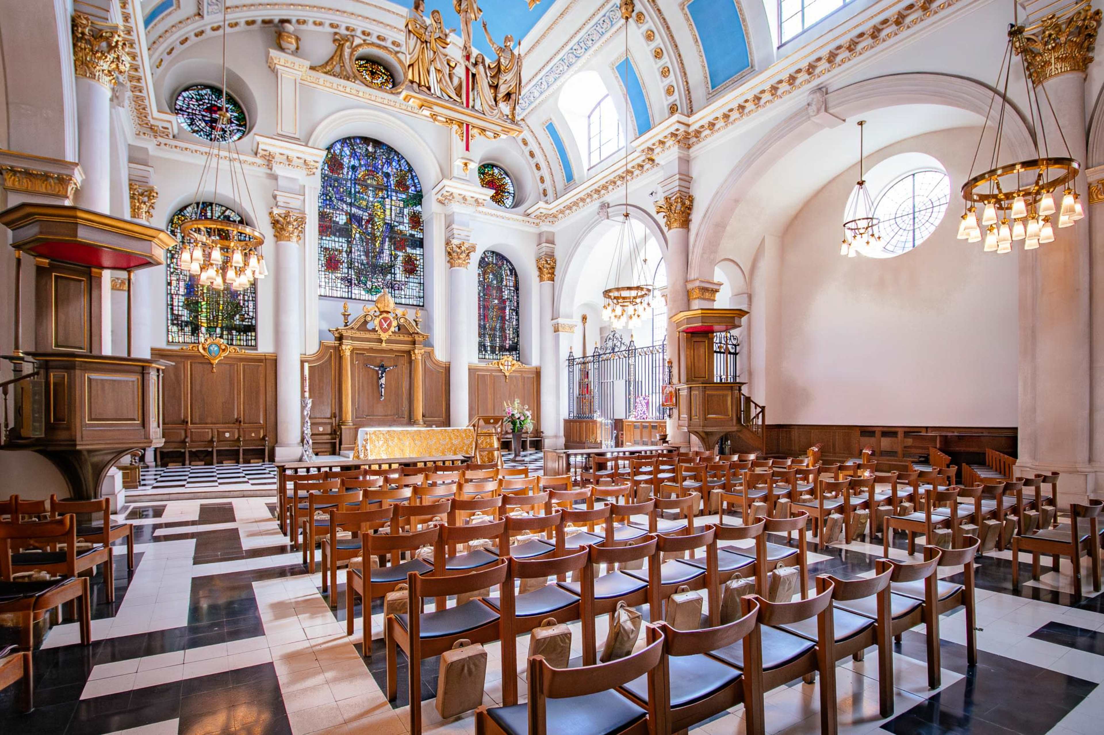 The interior of a church features rows of wooden chairs, a large altar, and stained glass windows illuminating the space.