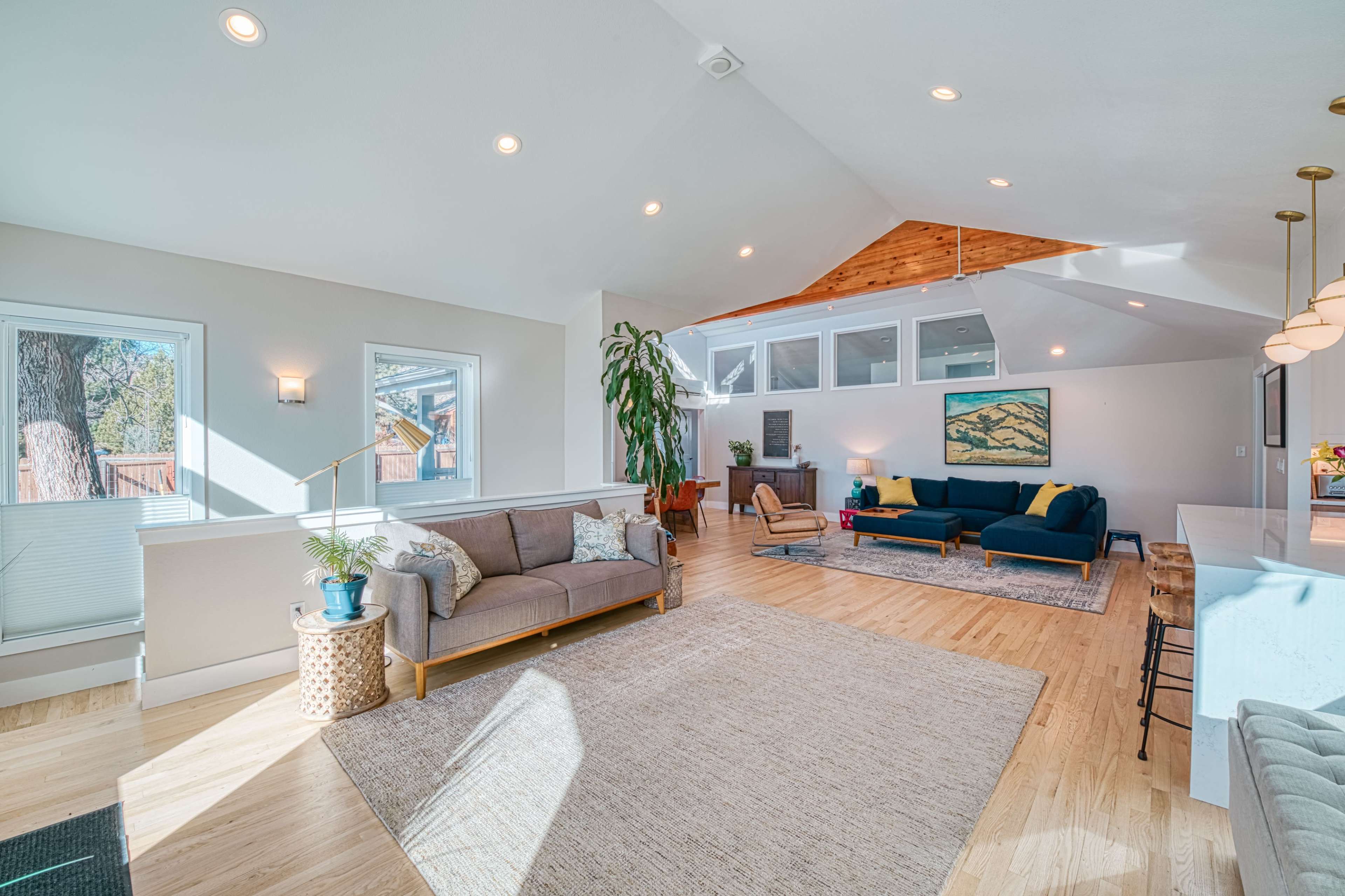 The bright, spacious interior features a living area with a sofa, armchair, and large windows, complemented by a light-colored rug and wooden accents.