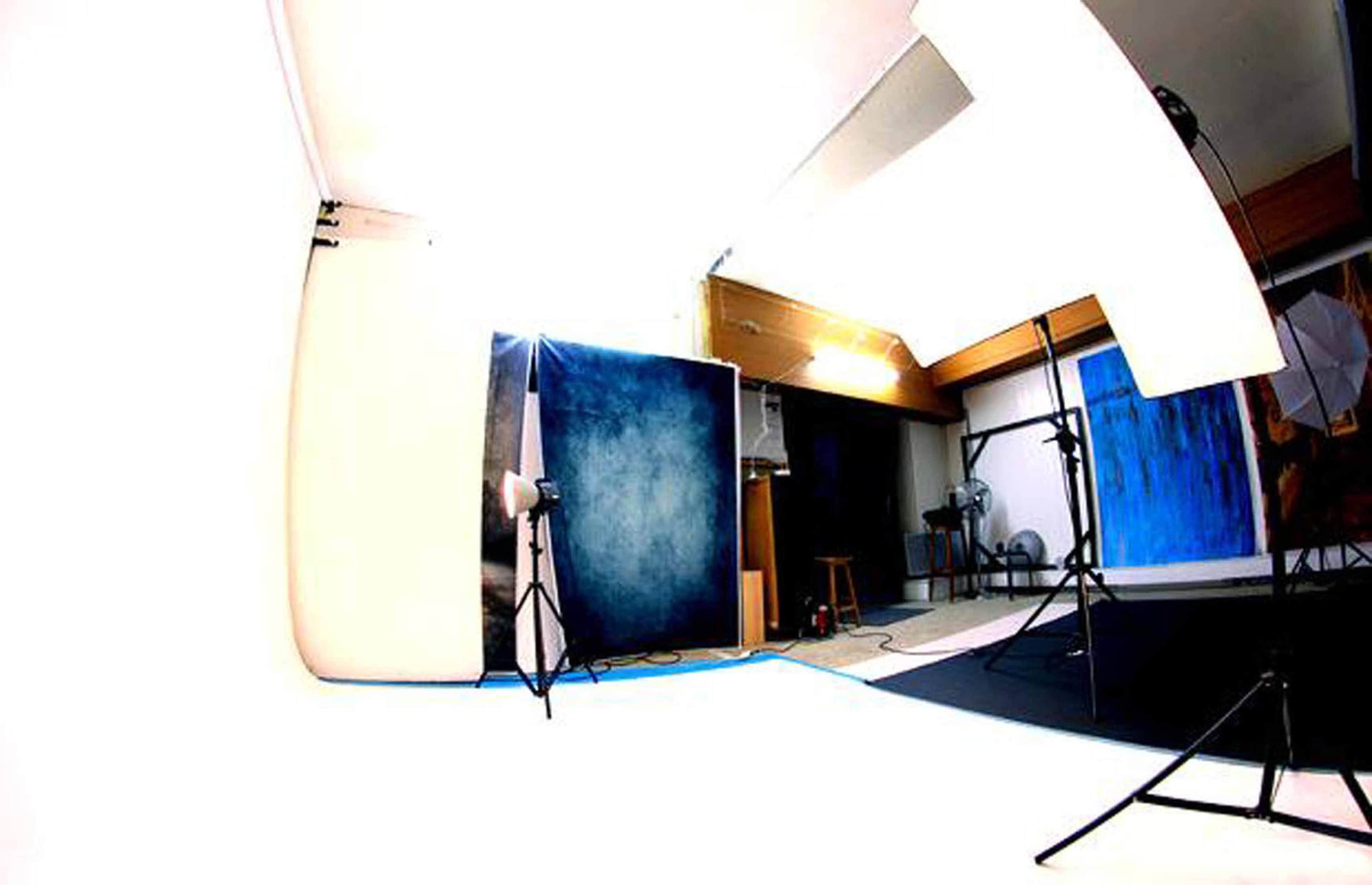 A photography studio with a blue backdrop, lighting equipment, and a stool in the corner.