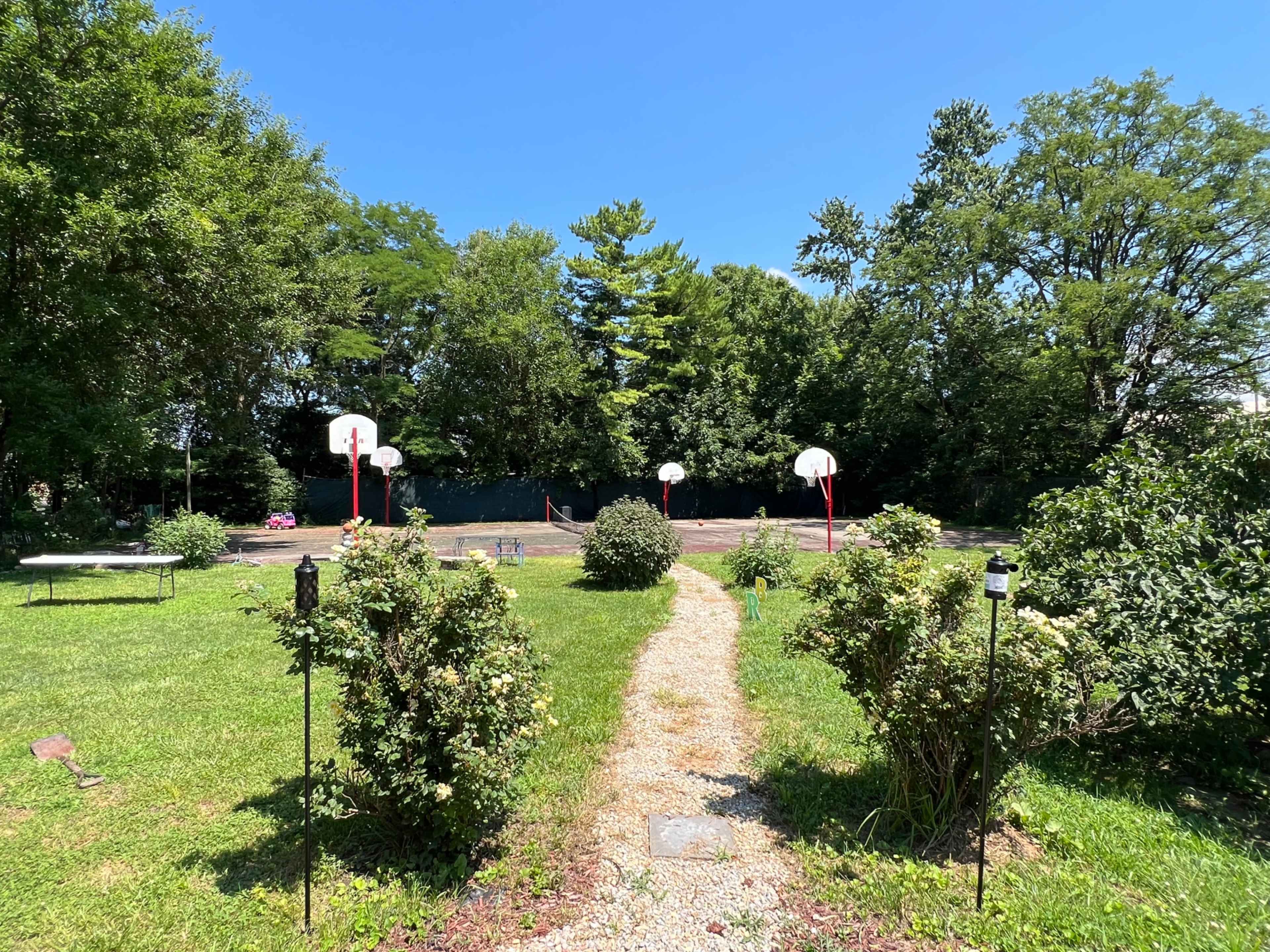 A gravel pathway leads through green grass to a basketball court with multiple hoops in a park-like setting.