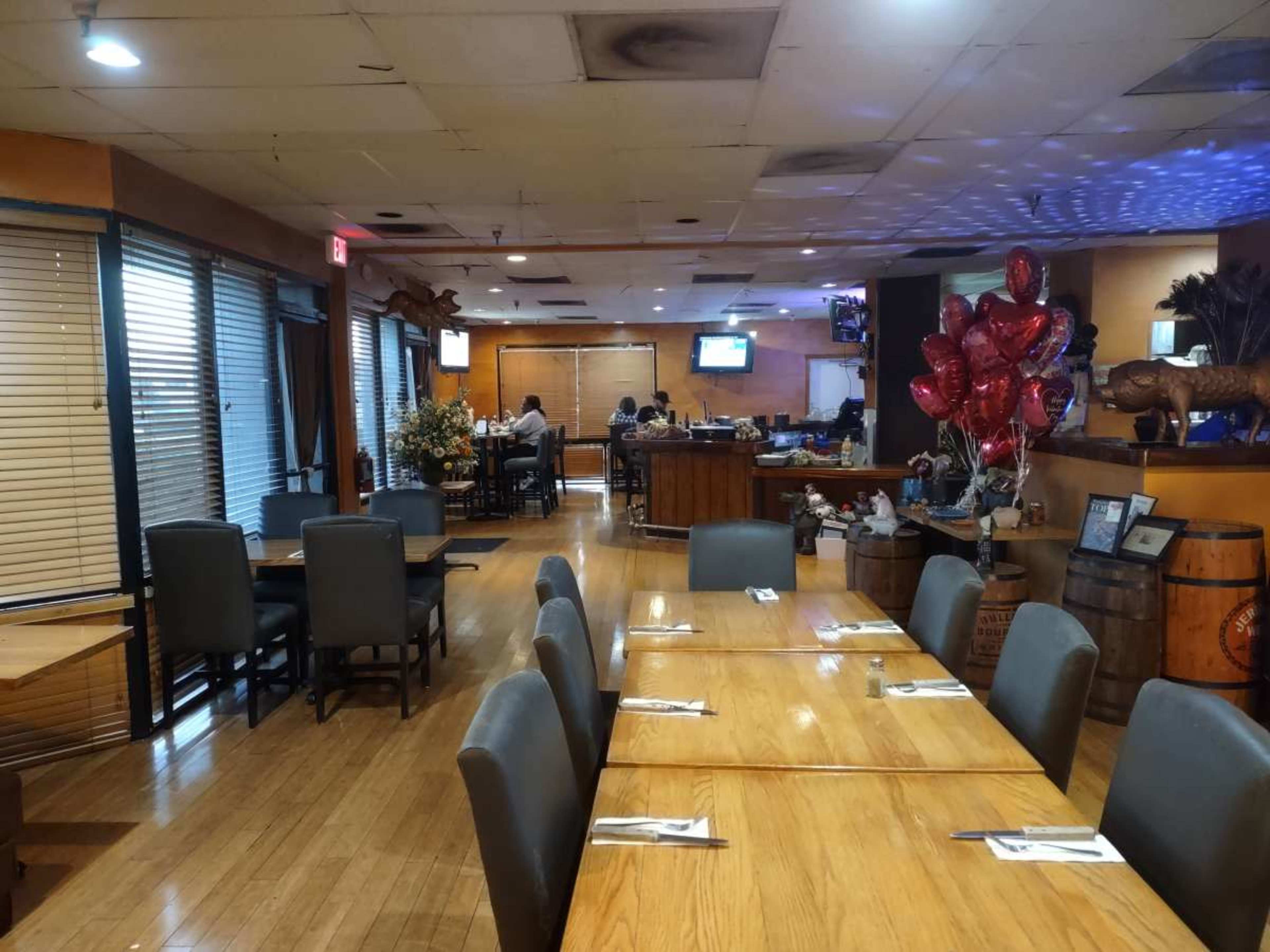 The image shows a spacious restaurant interior with wooden tables set for dining and a bar area in the background.