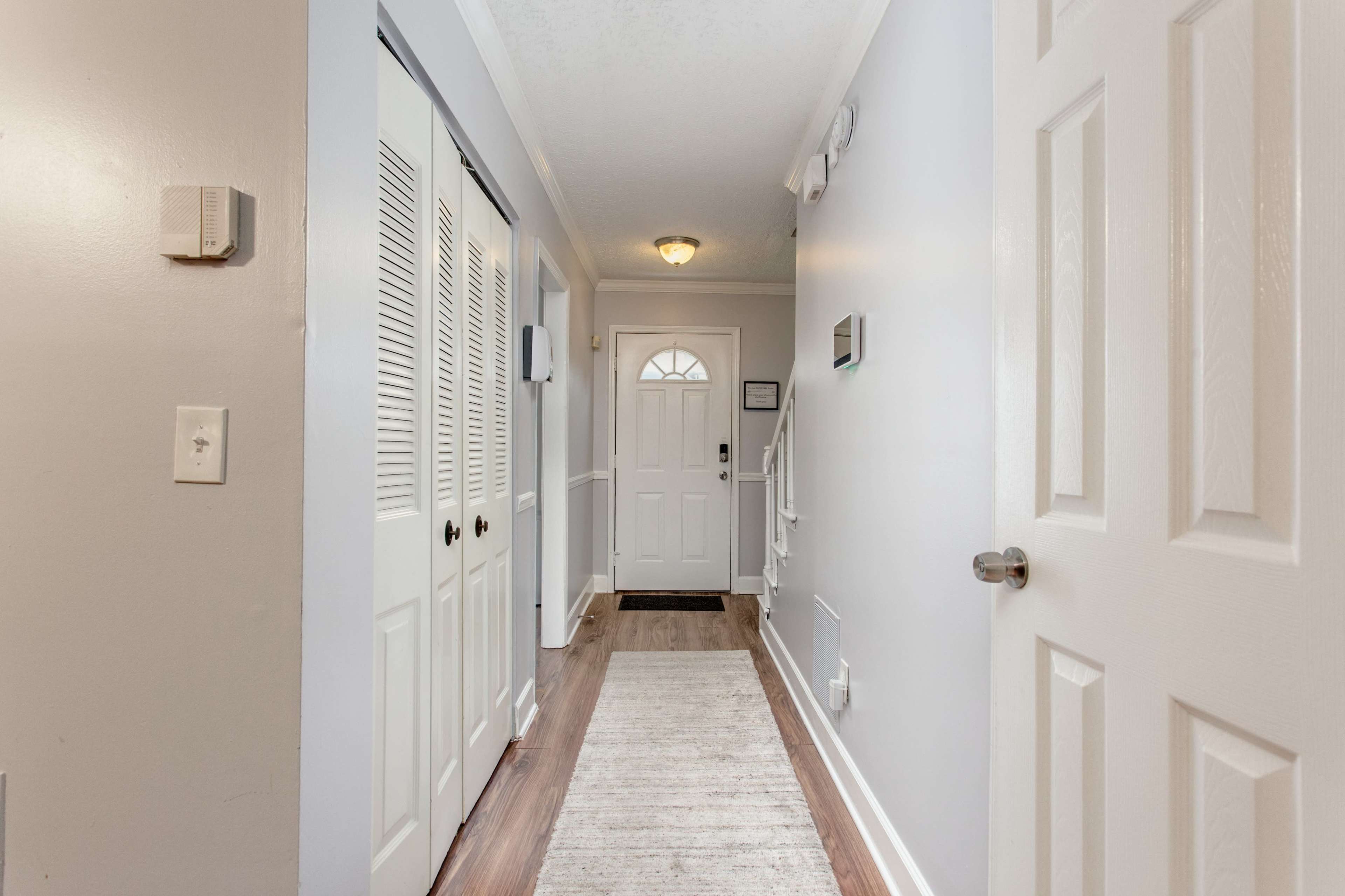 A hallway featuring a front door, white walls, a light fixture, and closet doors on one side.