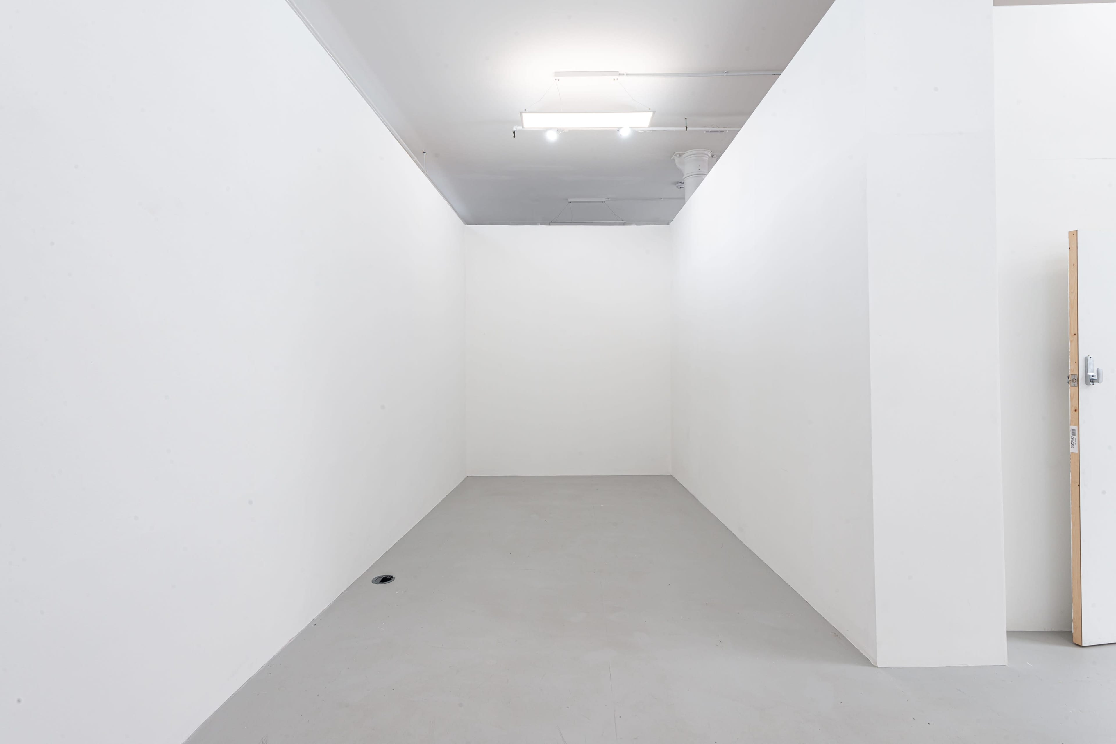 An empty, white-walled room with a concrete floor and a single light fixture on the ceiling.