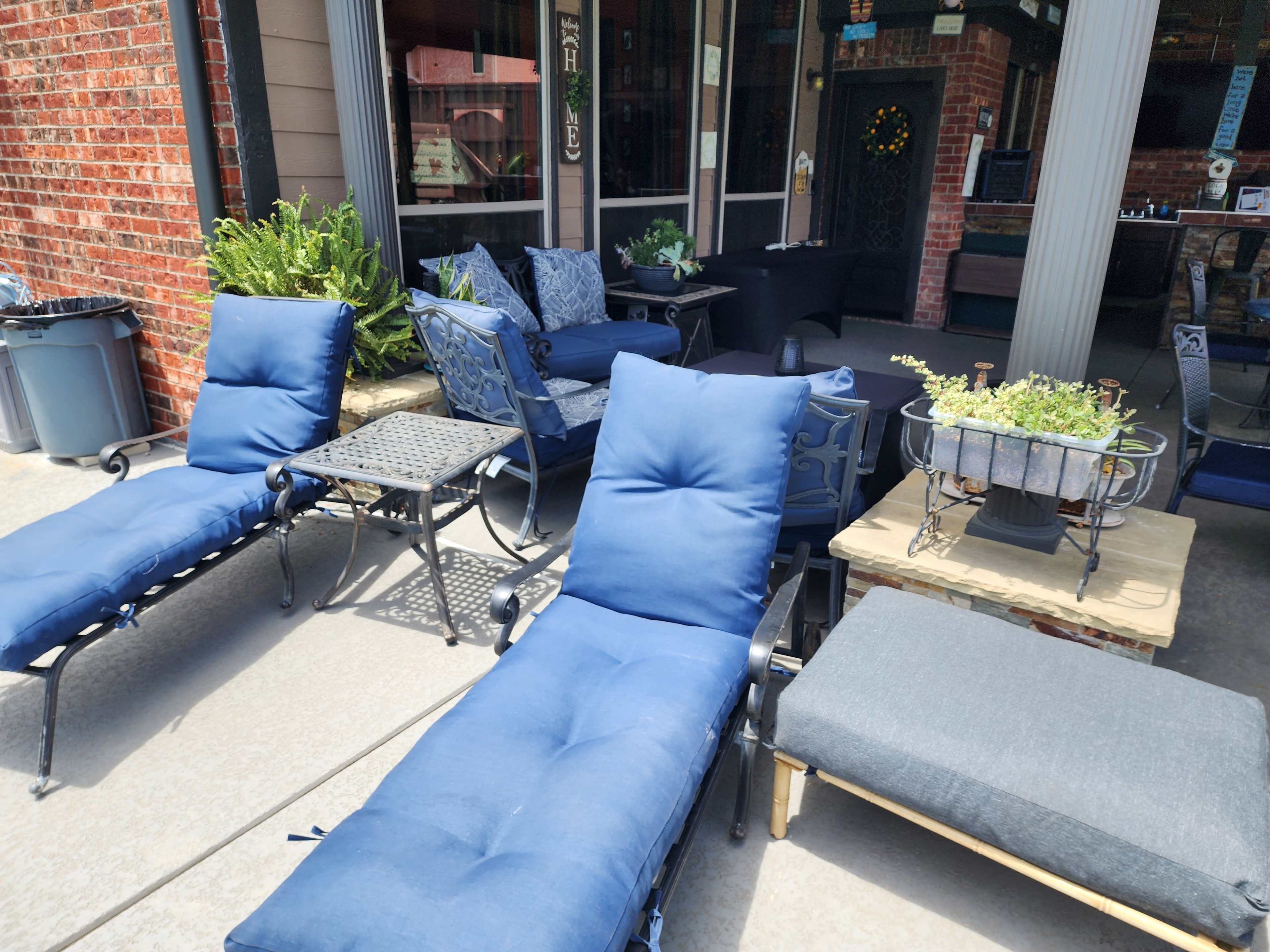 The scene features several navy blue lounge chairs and a small table arranged on a patio area, with a brick wall and potted plants in the background.