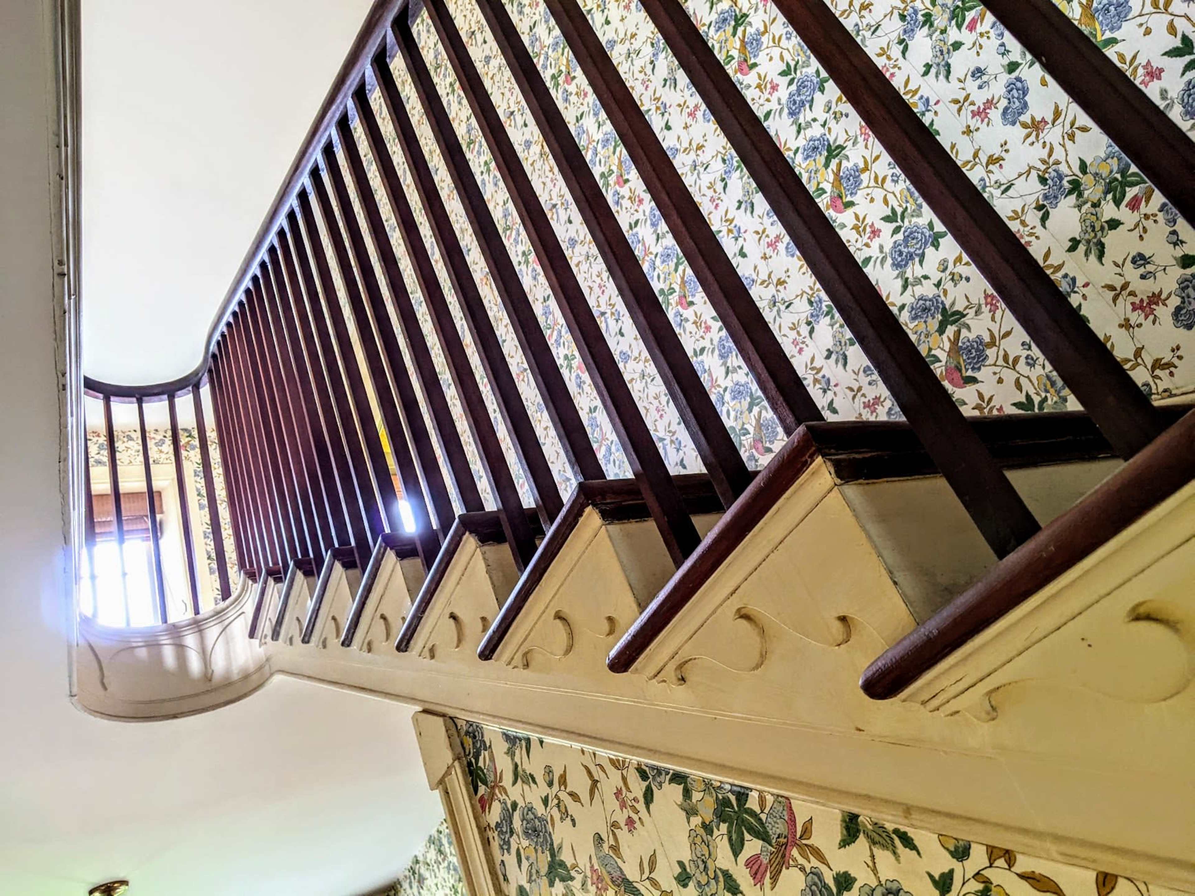 A winding staircase with wooden railings and floral wallpaper on the walls.