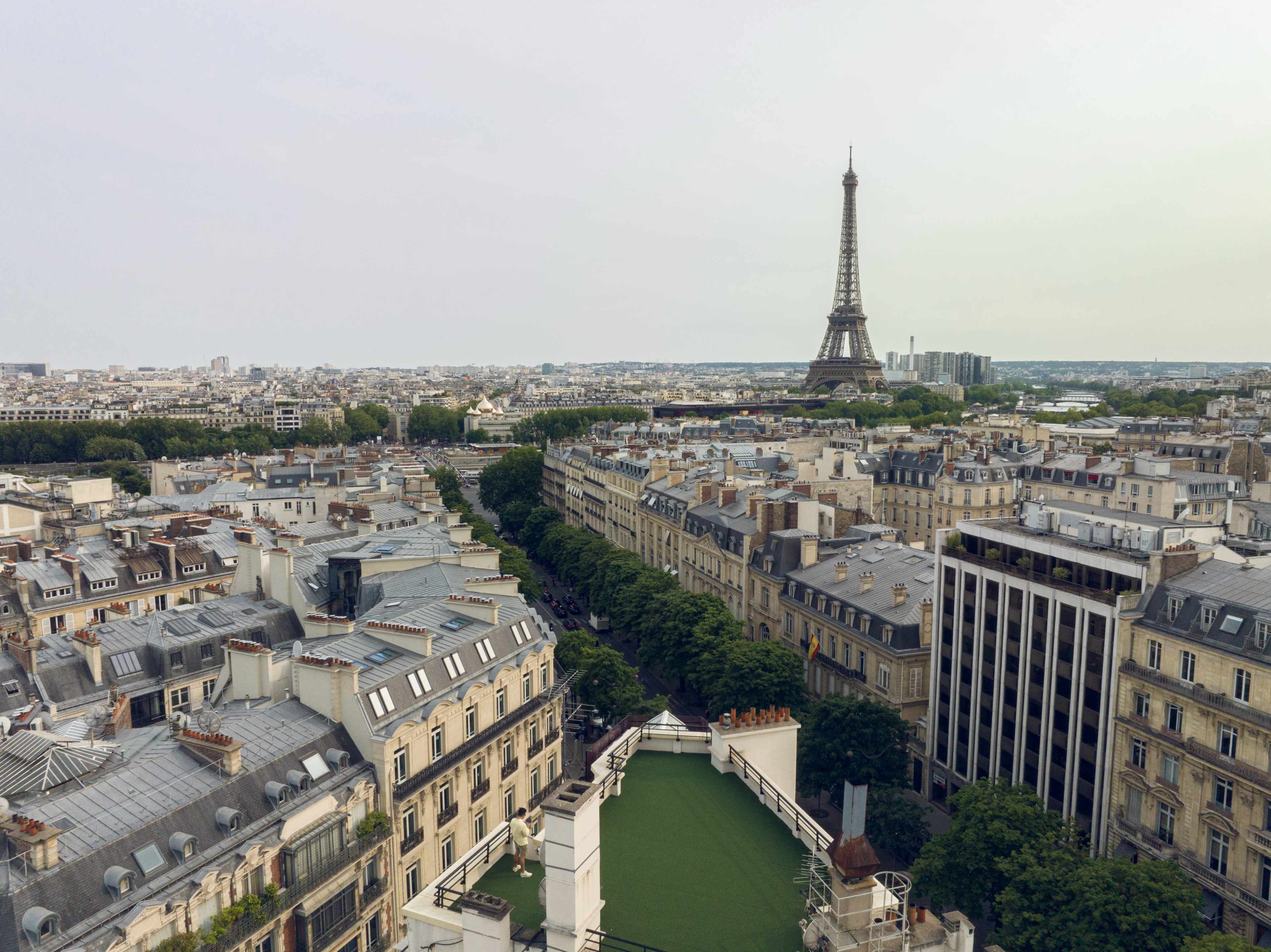 The image shows a panoramic view of Paris with the Eiffel Tower in the distance, surrounded by classic French architecture and tree-lined streets.