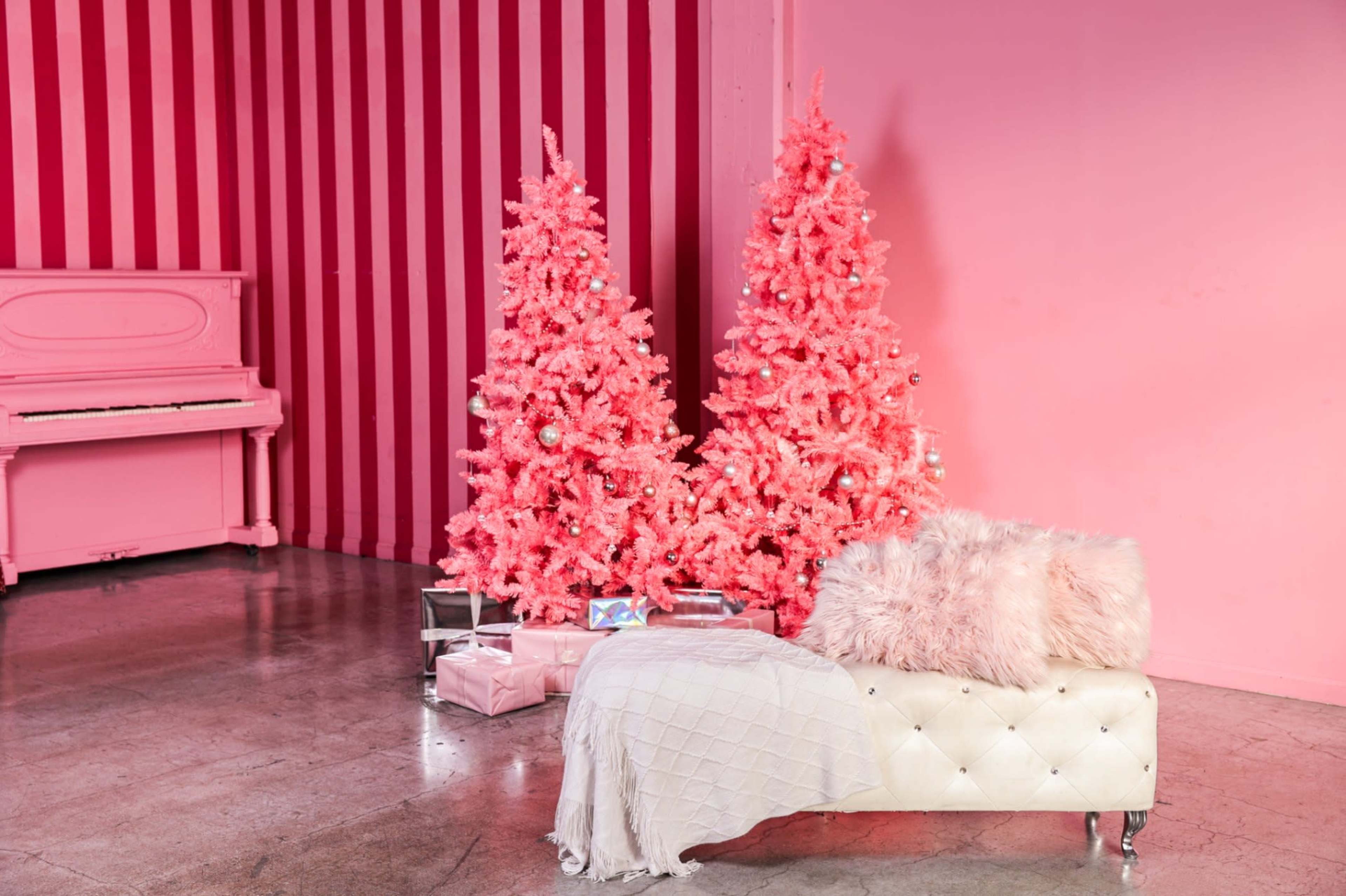 The image shows a bright pink room with two pink Christmas trees and a white tufted bench with a fluffy pink throw.