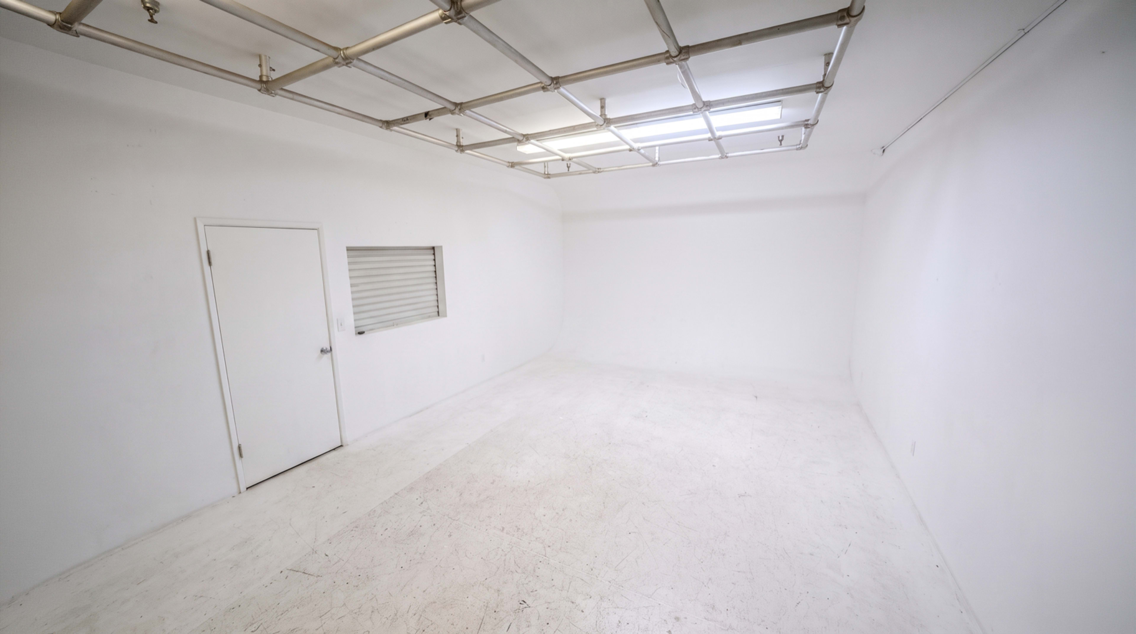 The image shows an empty, white-walled room with a door and a small window.