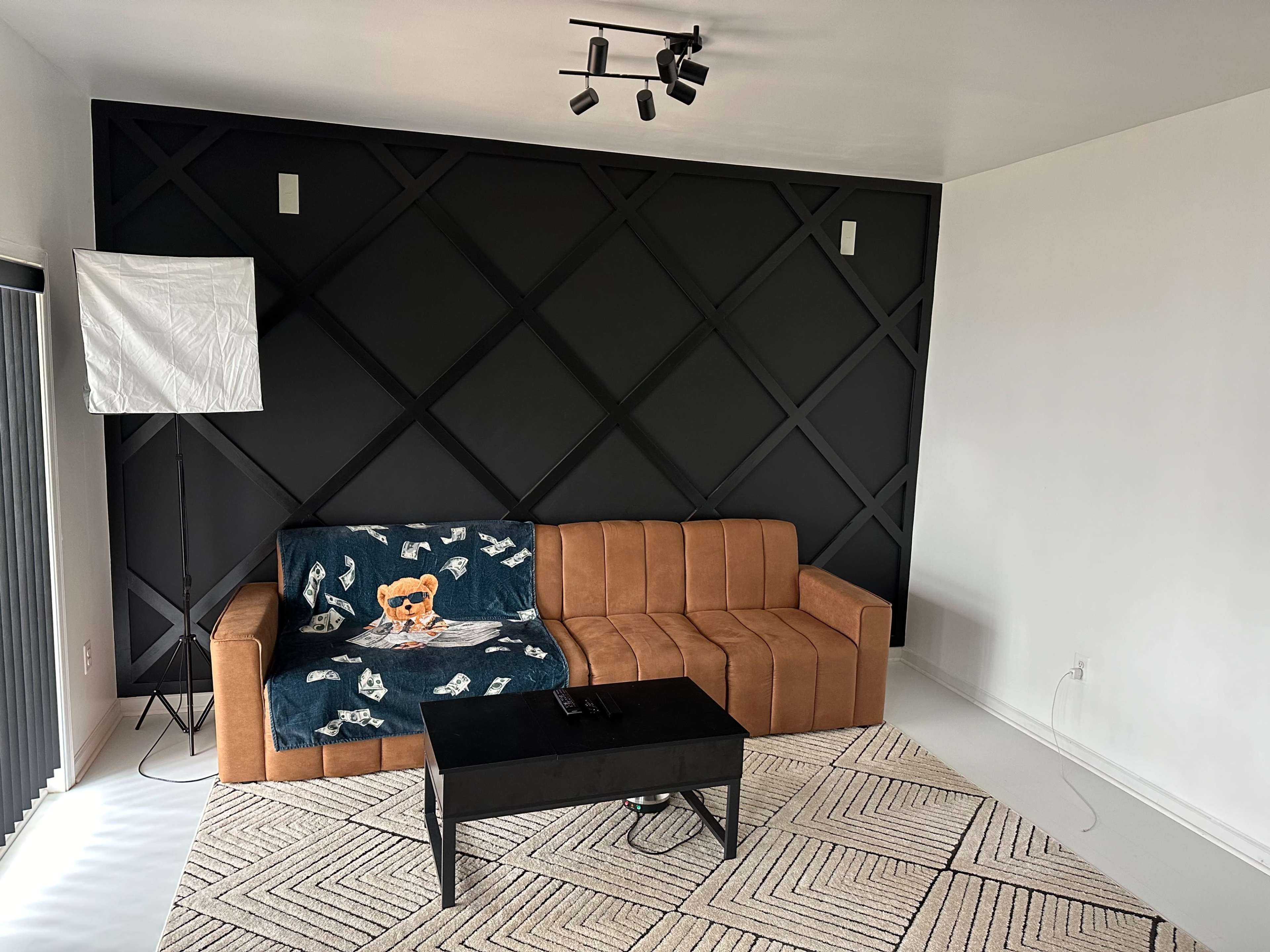 A modern living room with a brown couch, a black coffee table, and a decorative throw blanket featuring a dog design, set against a black patterned wall.