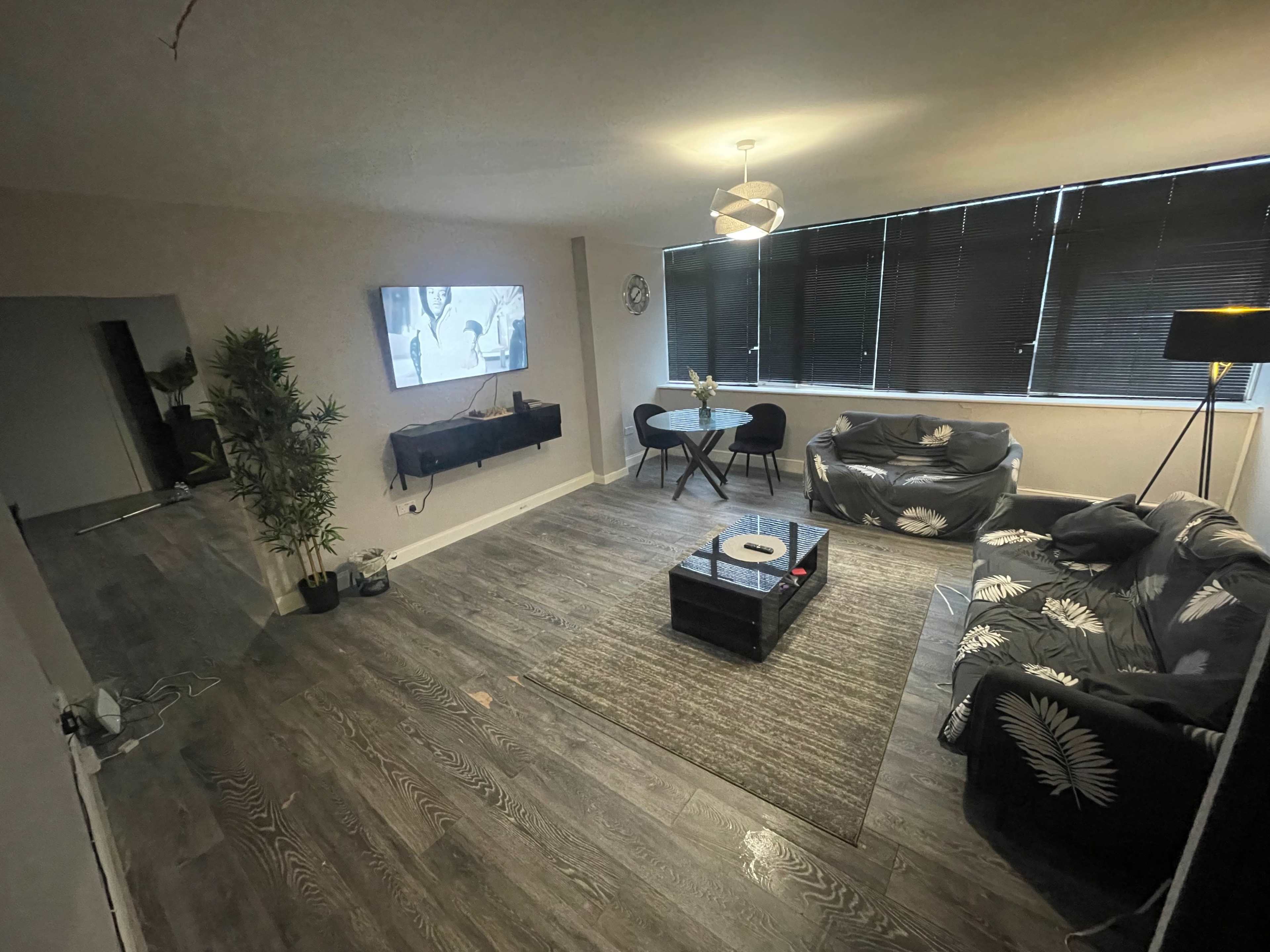 A modern living room with a large window, black couches, a coffee table, and a television mounted on the wall.