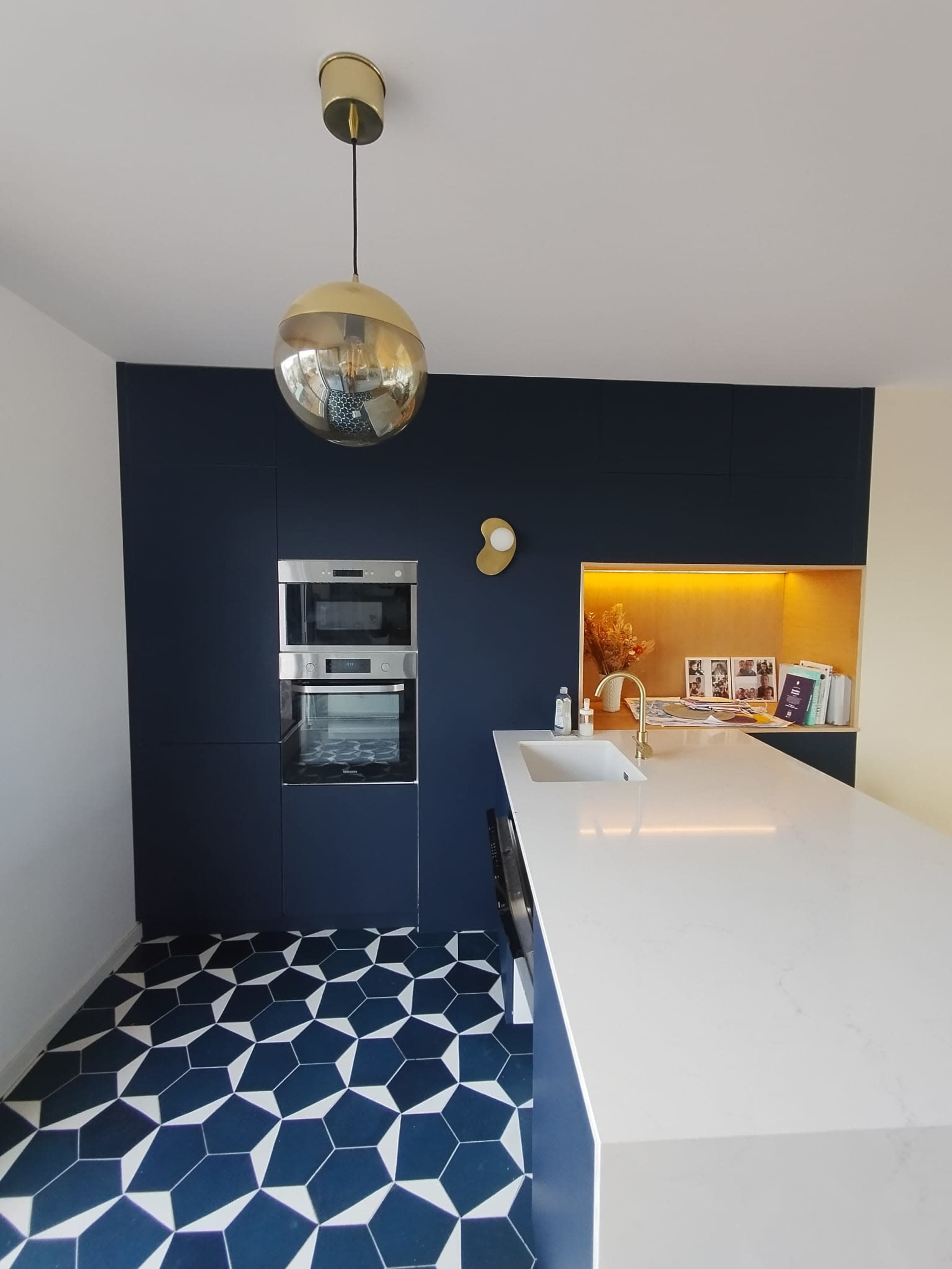 A modern kitchen featuring dark blue cabinetry, a white countertop, a built-in oven, and geometric patterned flooring.