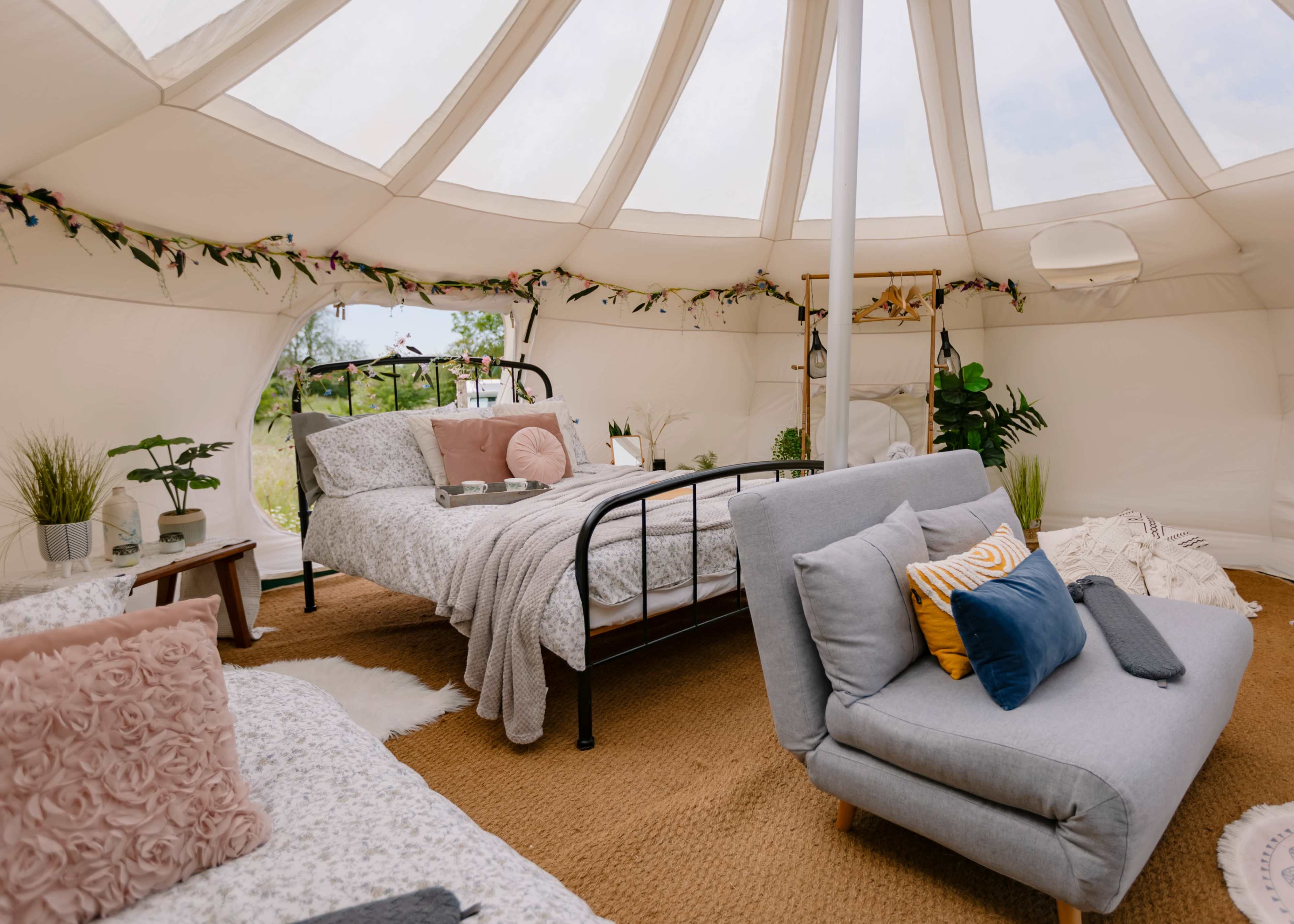 A comfortable, stylish yurt interior featuring two beds, a cozy seating area, and decorative plants.