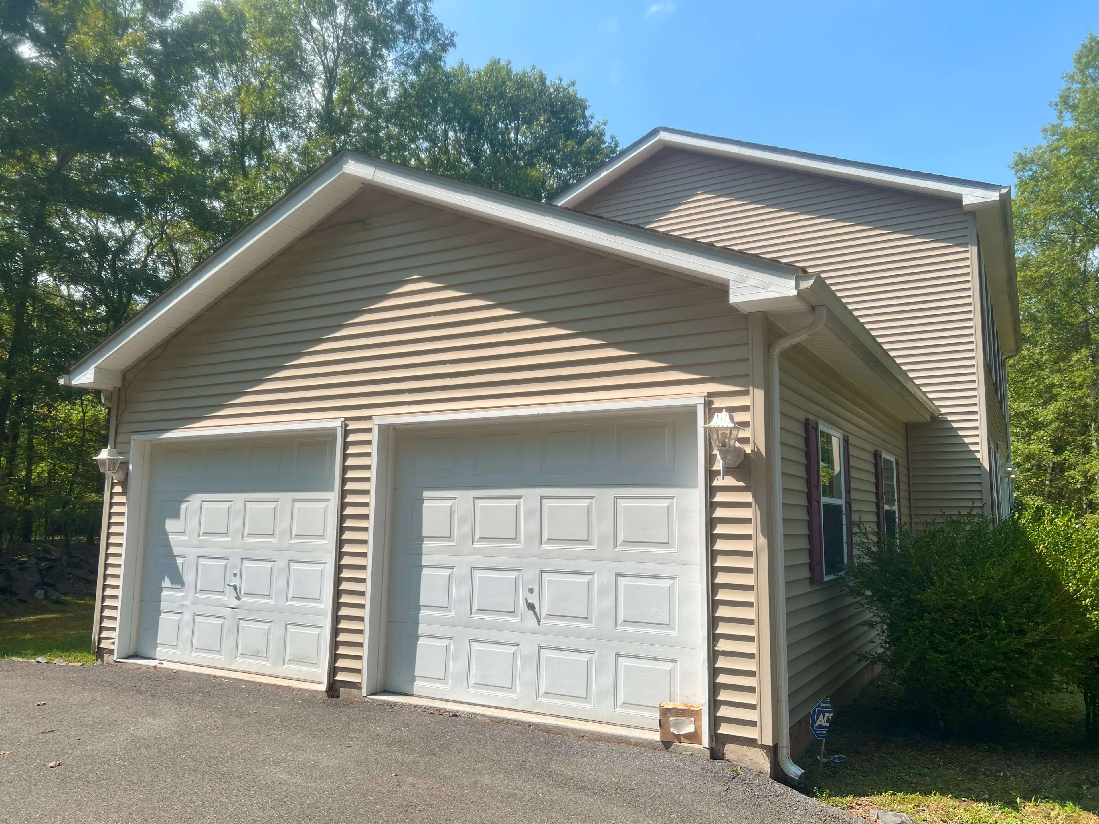 A two-car garage with white doors is attached to a beige house surrounded by trees.