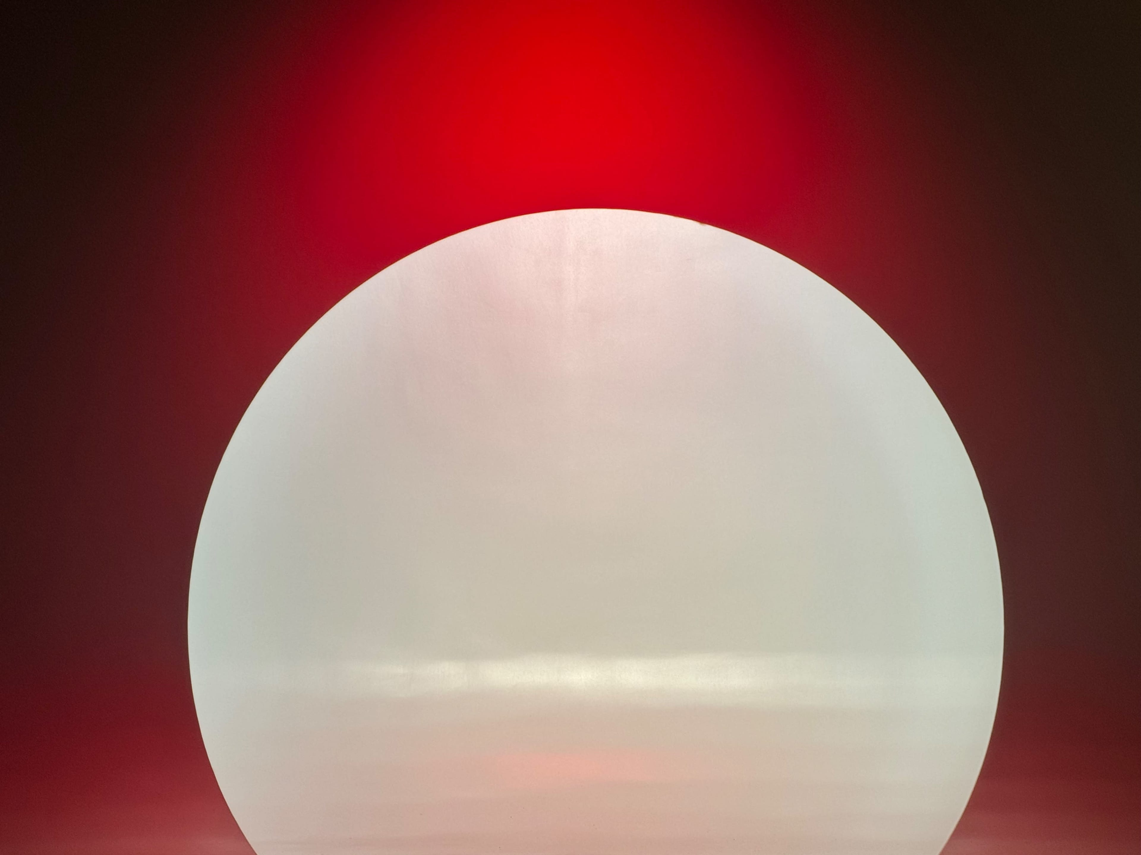 A large, semi-transparent orb is set against a red background, casting soft reflections on the surface below.