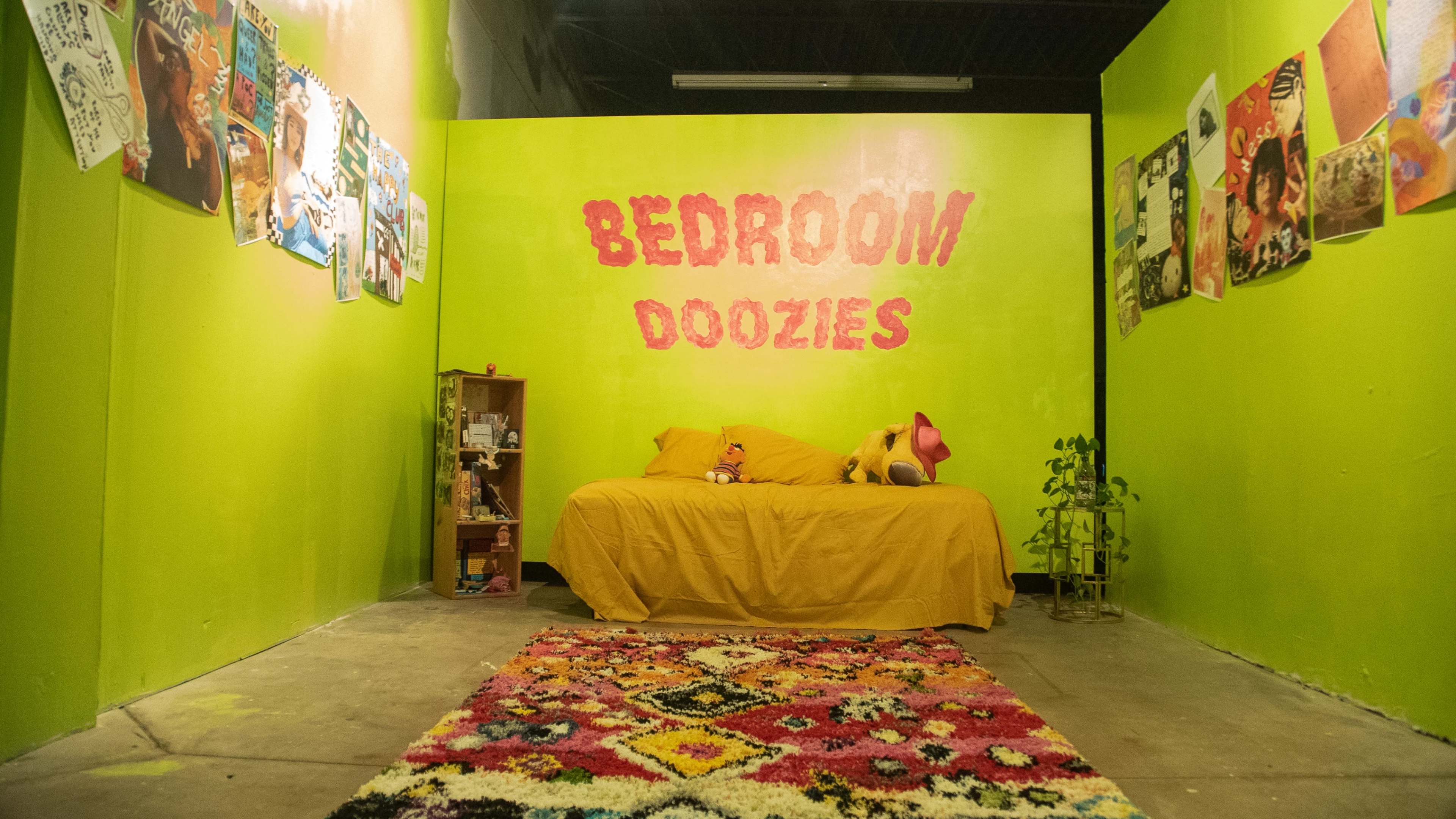 The image shows a small room with bright green walls, a yellow bedspread, a colorful patterned rug, and posters adorning the walls.
