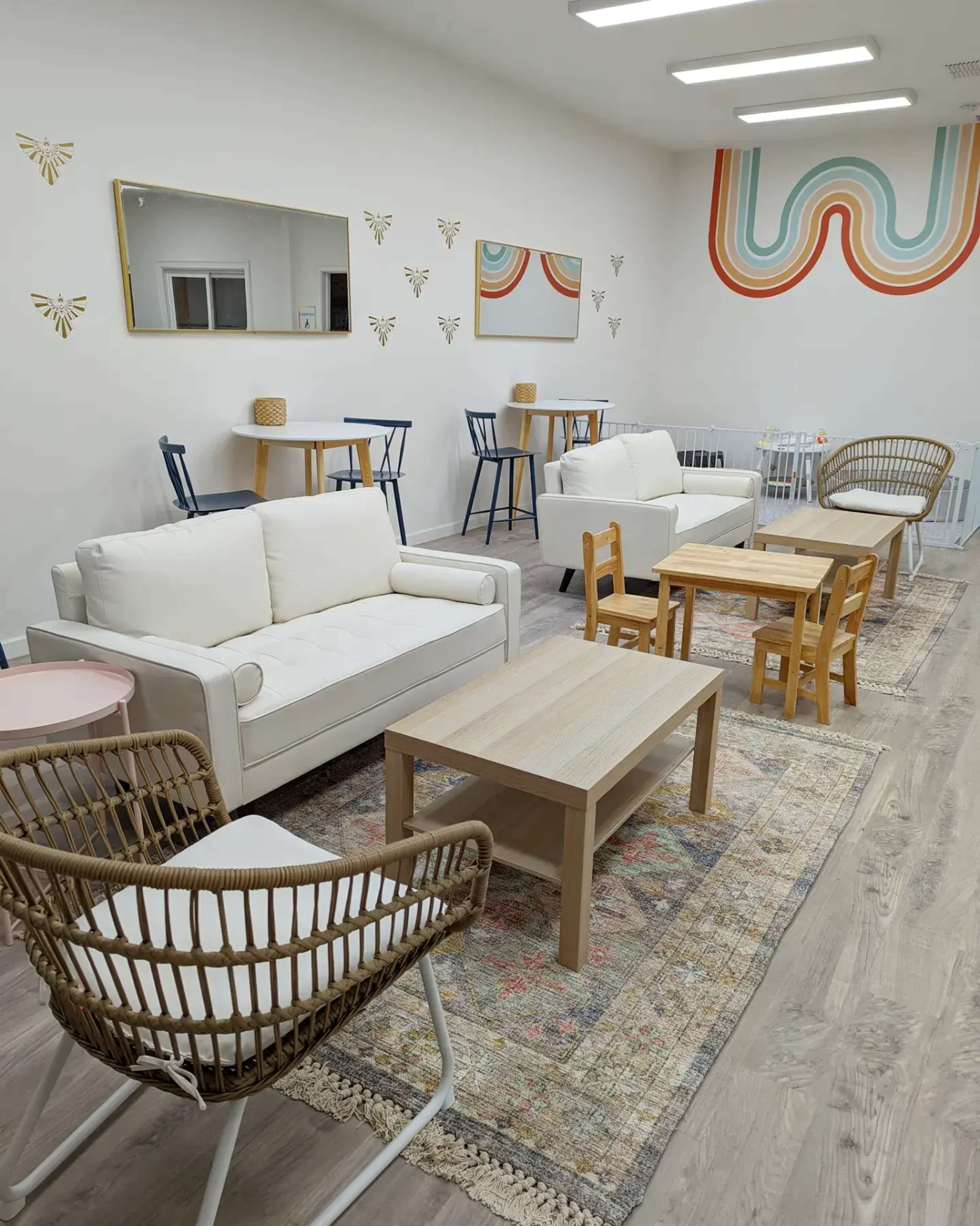 A cozy room features several pieces of modern furniture, including white sofas, wooden tables, and colorful chairs, arranged on a patterned rug.