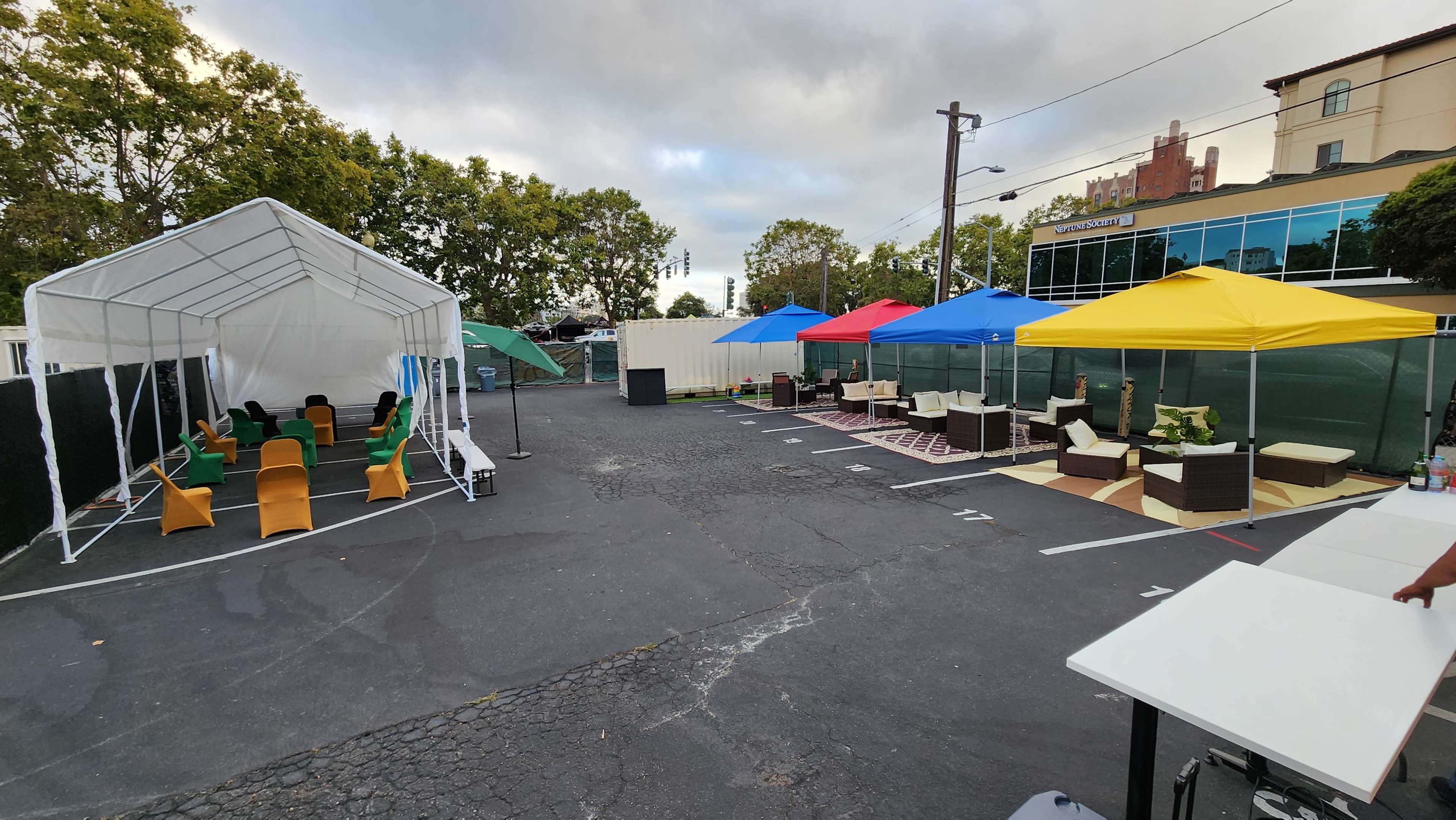 A parking area set up with various colorful tents, seating arrangements, and a backdrop of trees and a building.